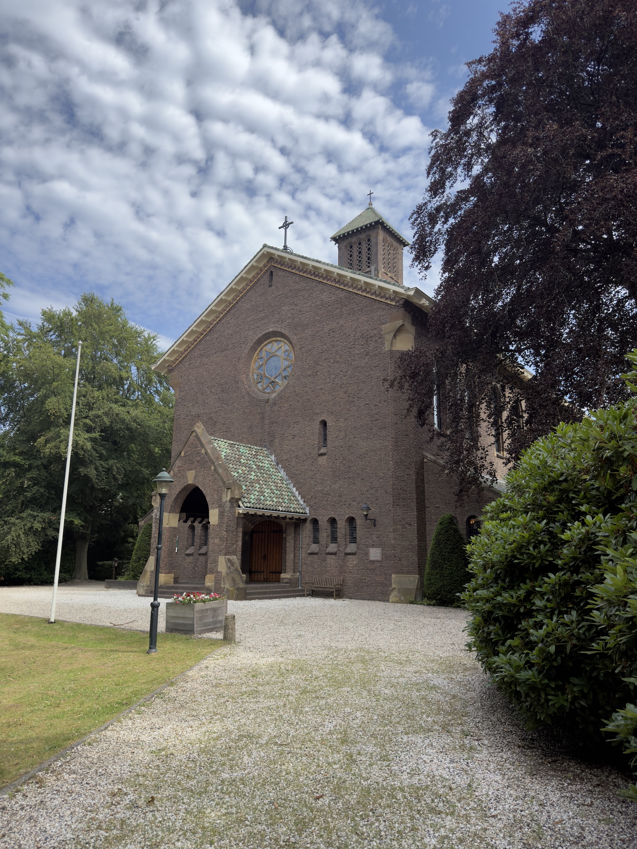 Brick chapel with a small bell tower and tiled porch beside a gravel path.
