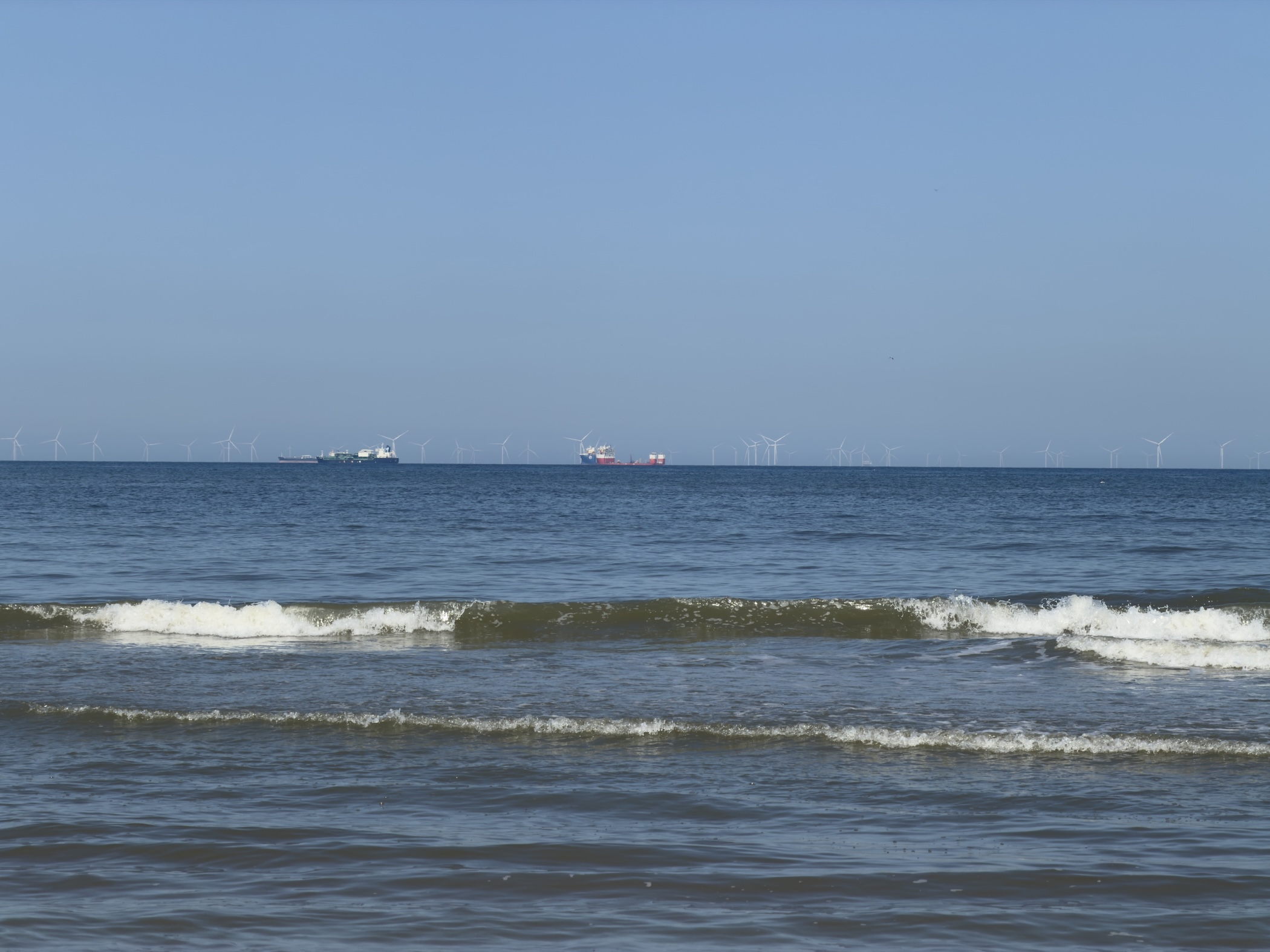 View across the North Sea with distant cargo ships and offshore wind turbines.