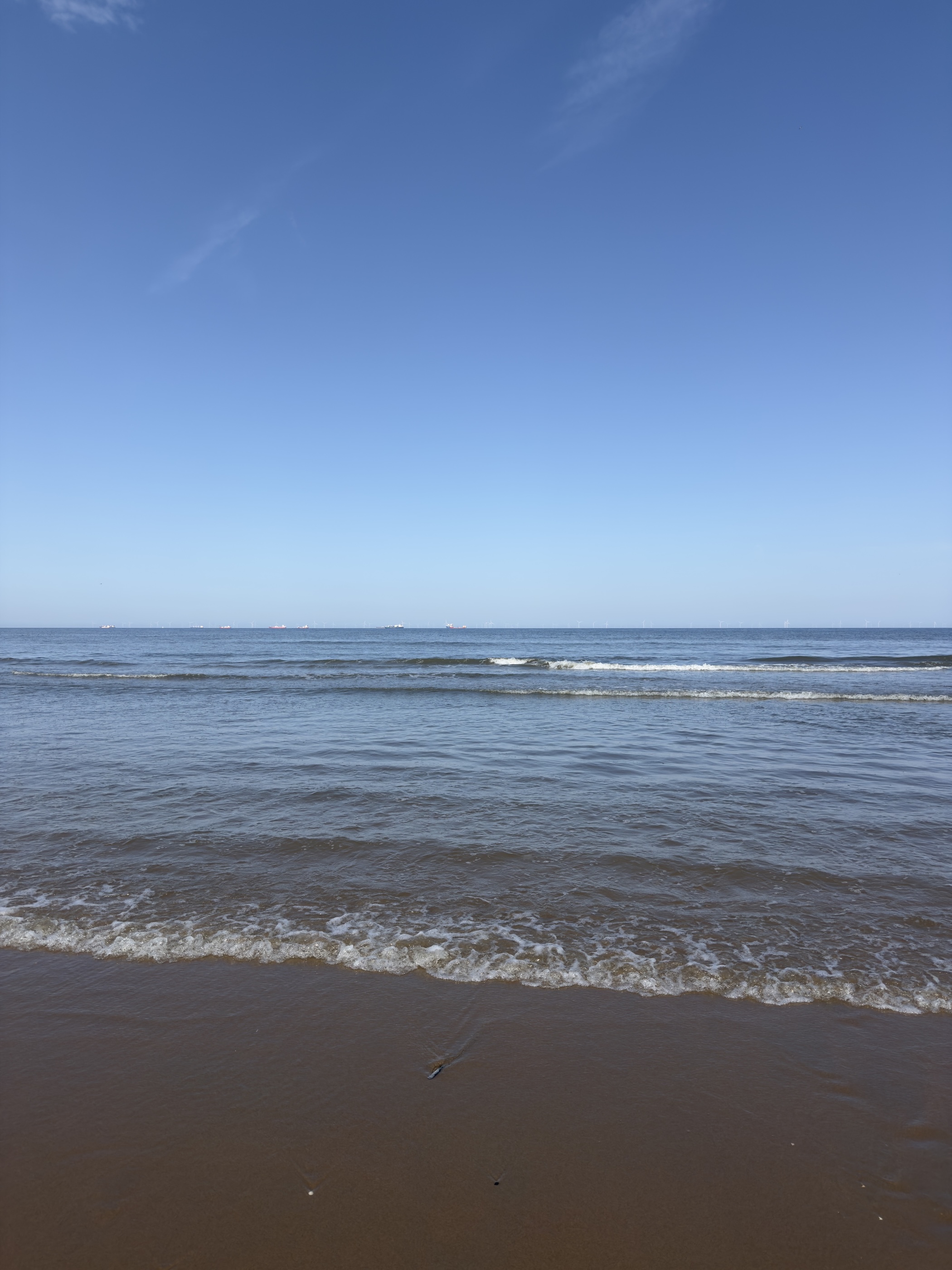 Gentle waves rolling onto wet brown sand under a clear blue sky.