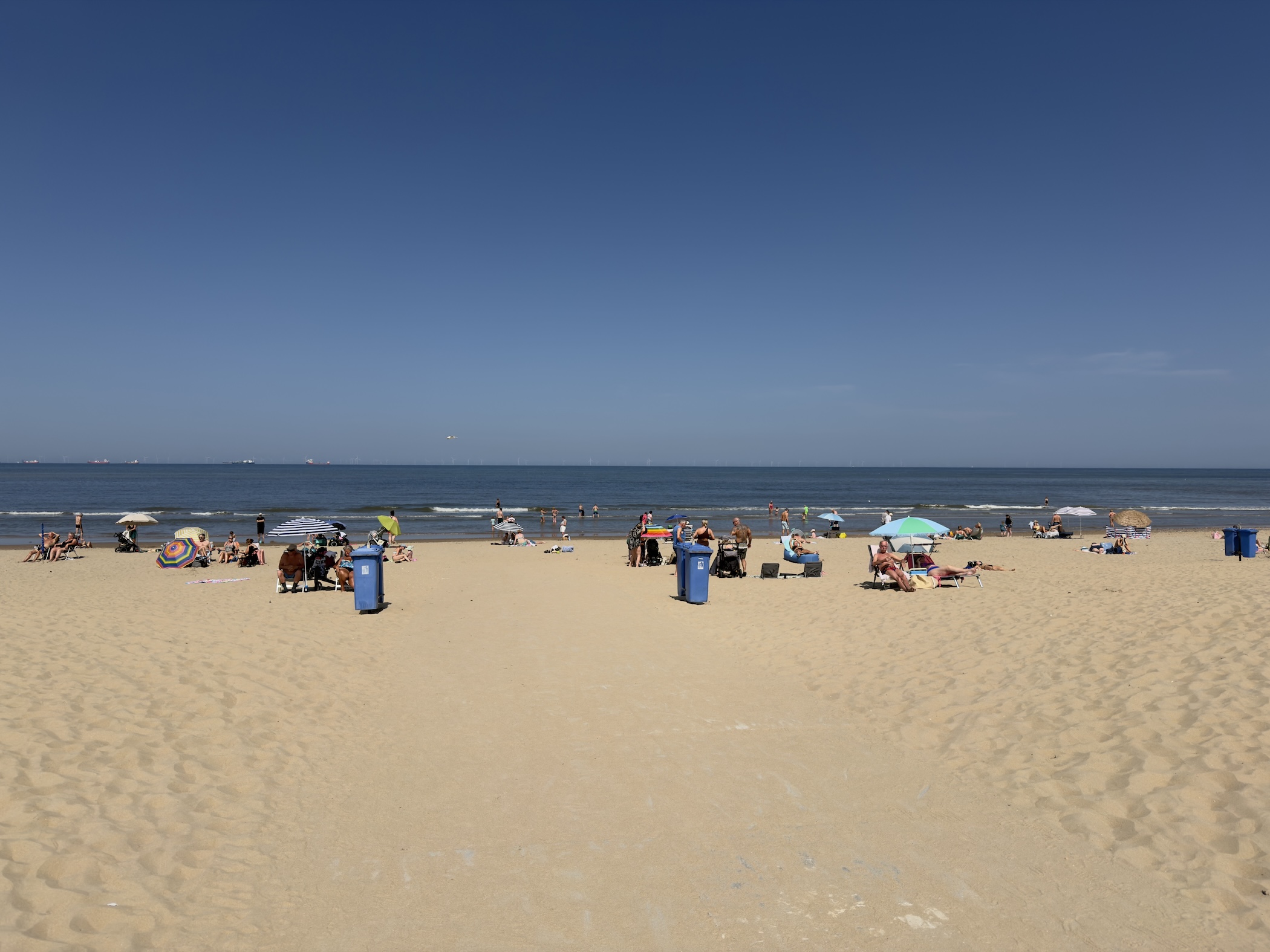 A broad sandy beach with sunbathers, umbrellas and bins beside the sea.