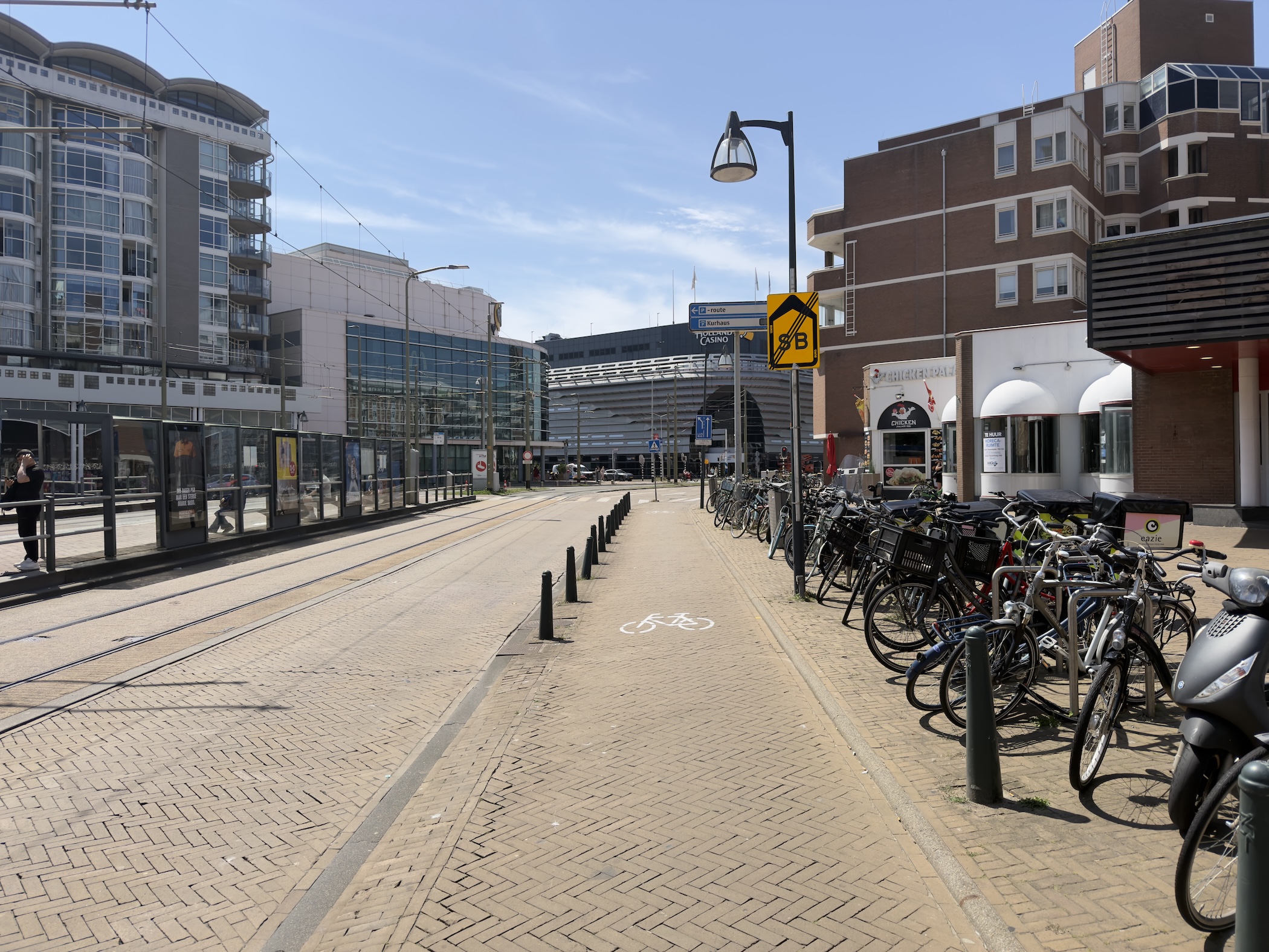 An empty city square with tram tracks, a cycle lane and rows of parked bicycles by tall buildings.