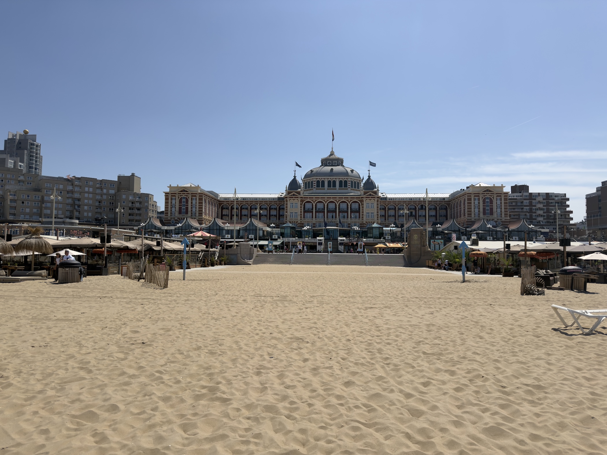Footprinted sand stretches towards the ornate Kurhaus hotel framed by beach bar parasols.