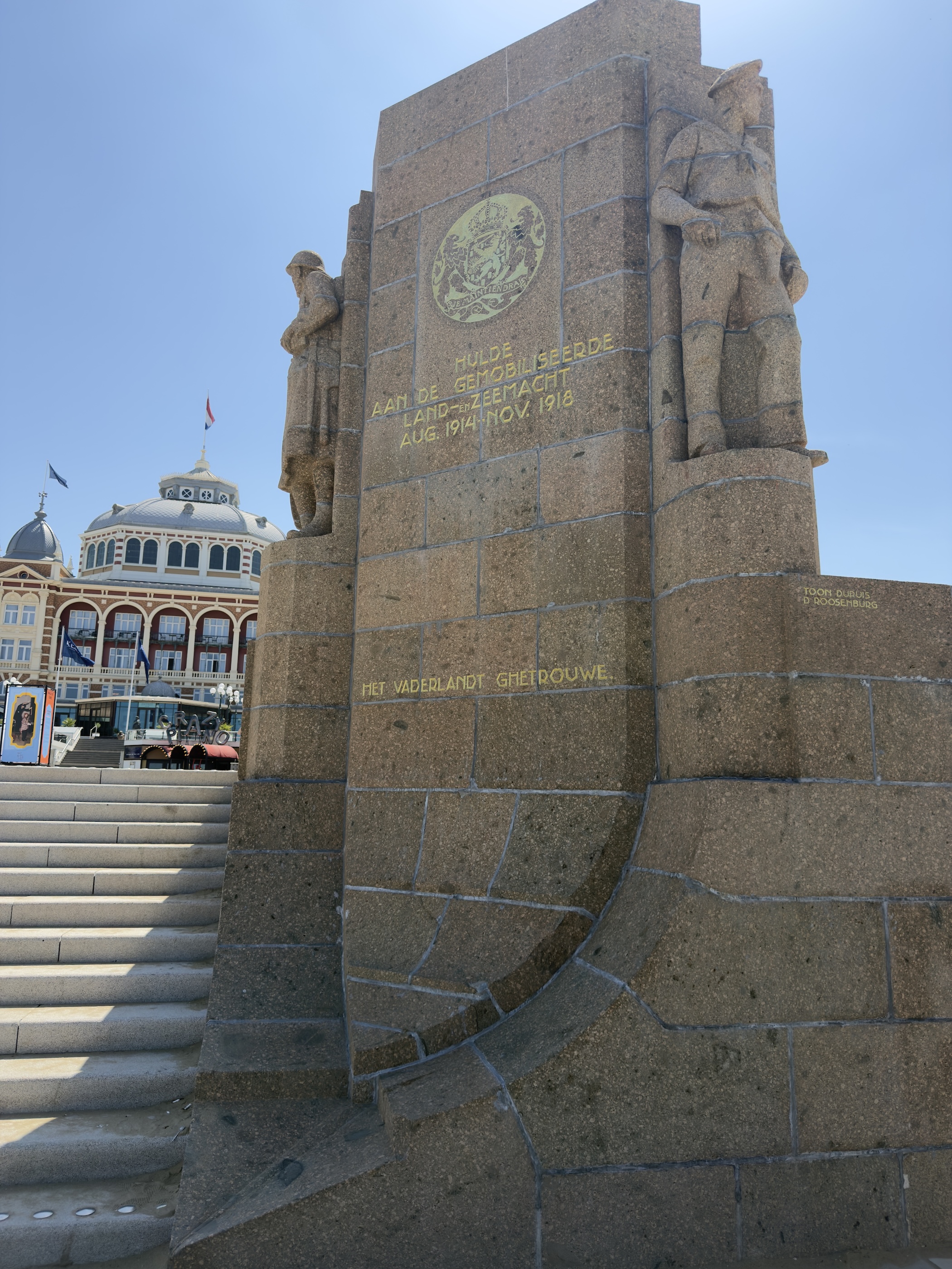 Stone war memorial with carved soldiers beside the domed Kurhaus building at Scheveningen.