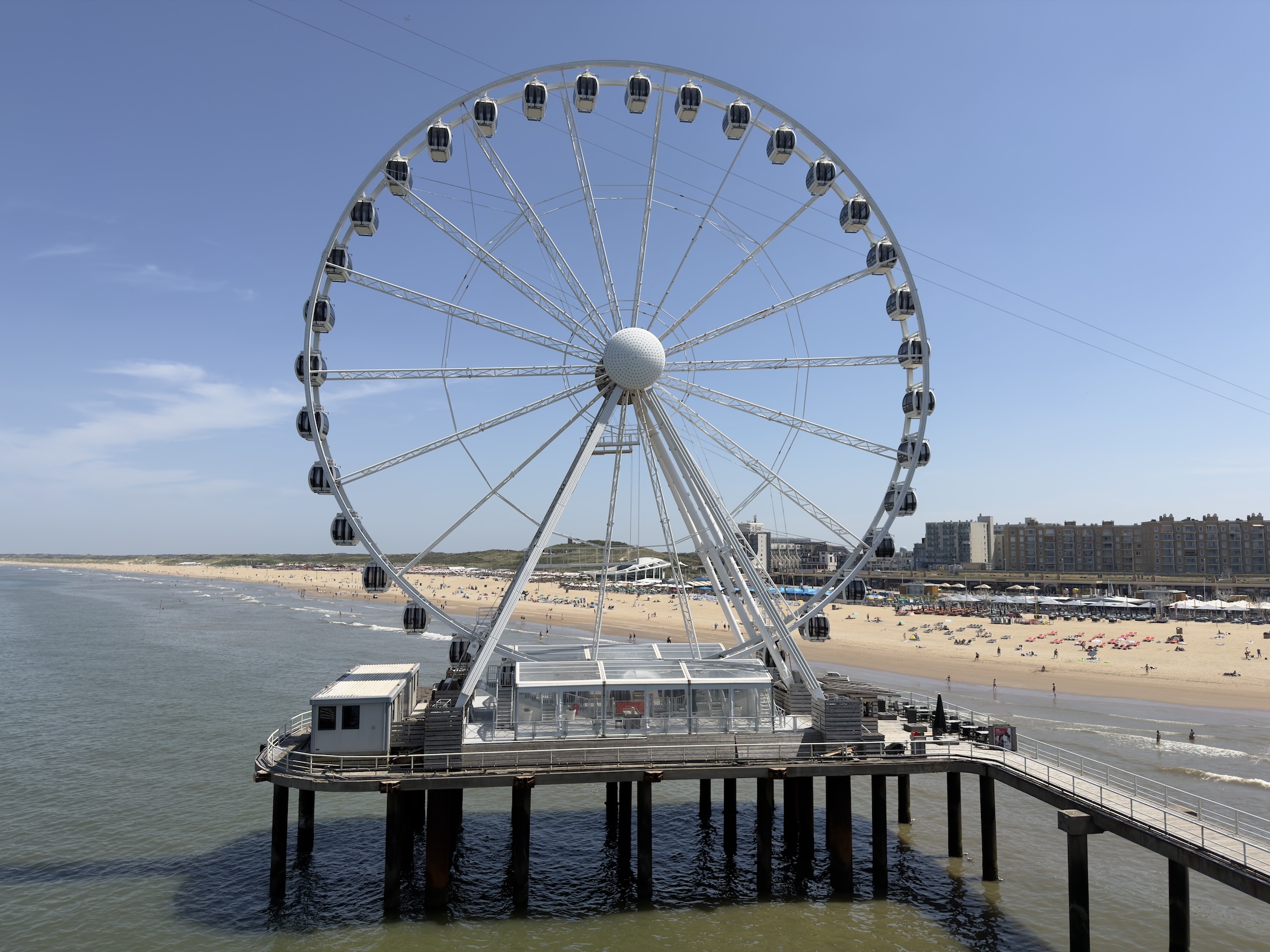 Large white Ferris wheel mounted on the pier above the beach, town and coastline behind.