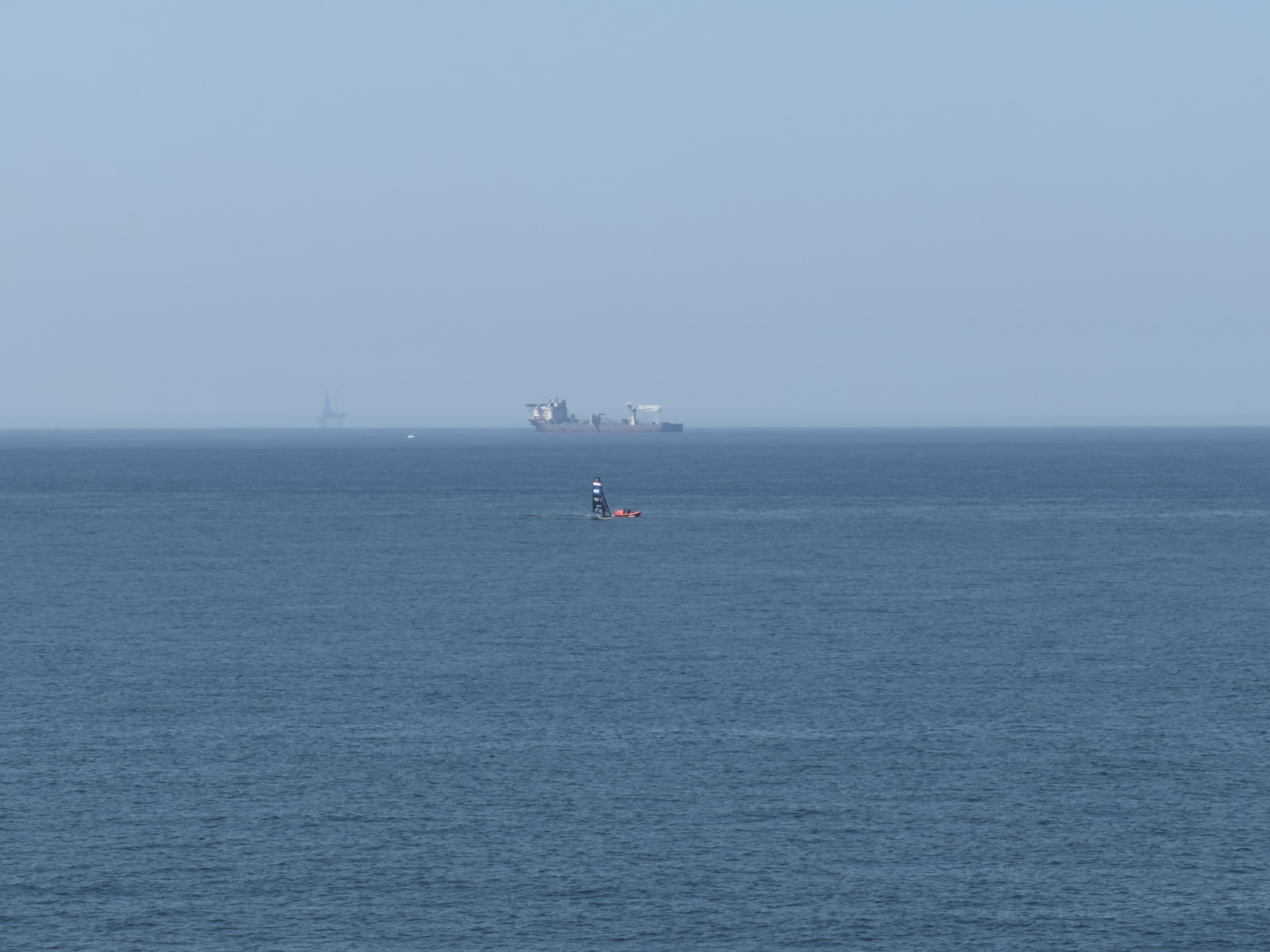 Hazy horizon over the North Sea with a cargo ship, distant rig and small orange boat.