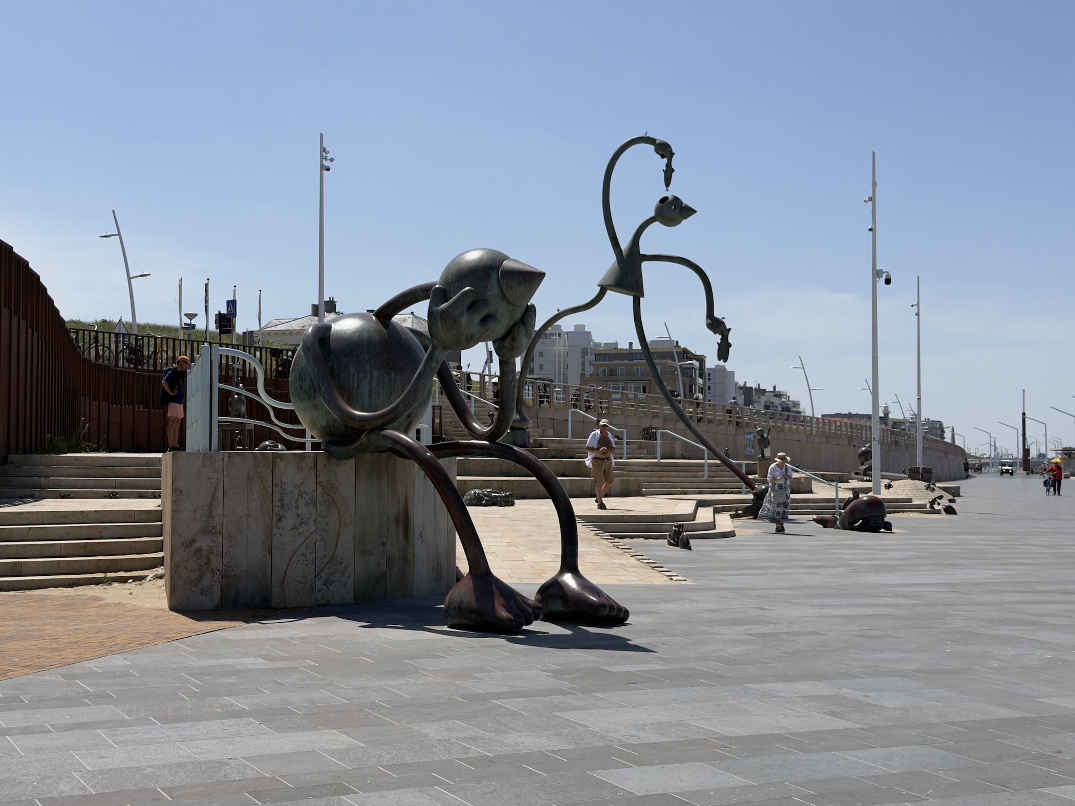 Whimsical bronze creature sculpture sprawled beside steps on the tiled seafront promenade.