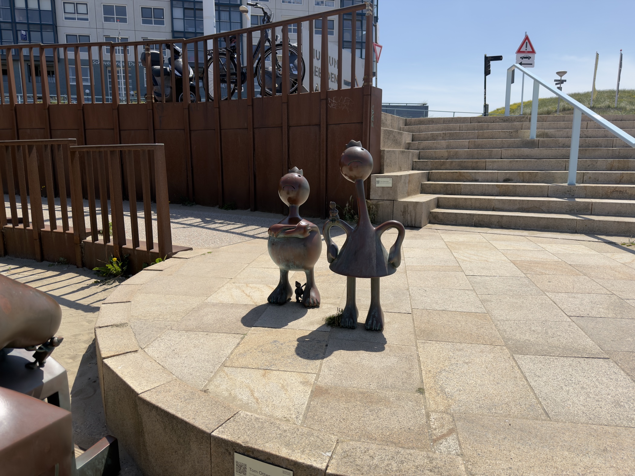 Two playful bronze bird-like sculptures on a stone plaza beside steps and railings.