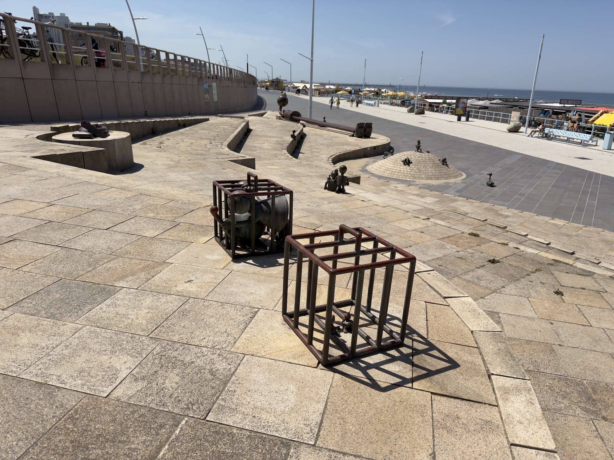 Open promenade with metal cage artworks and scattered sculptures running down to the sea.