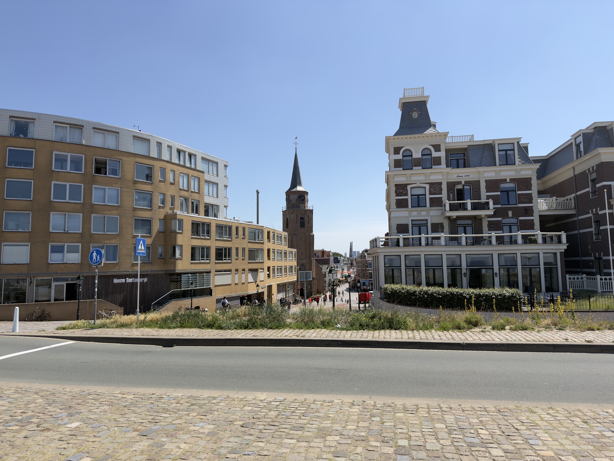 Resort buildings and a church spire seen across a cobbled road under a clear sky.