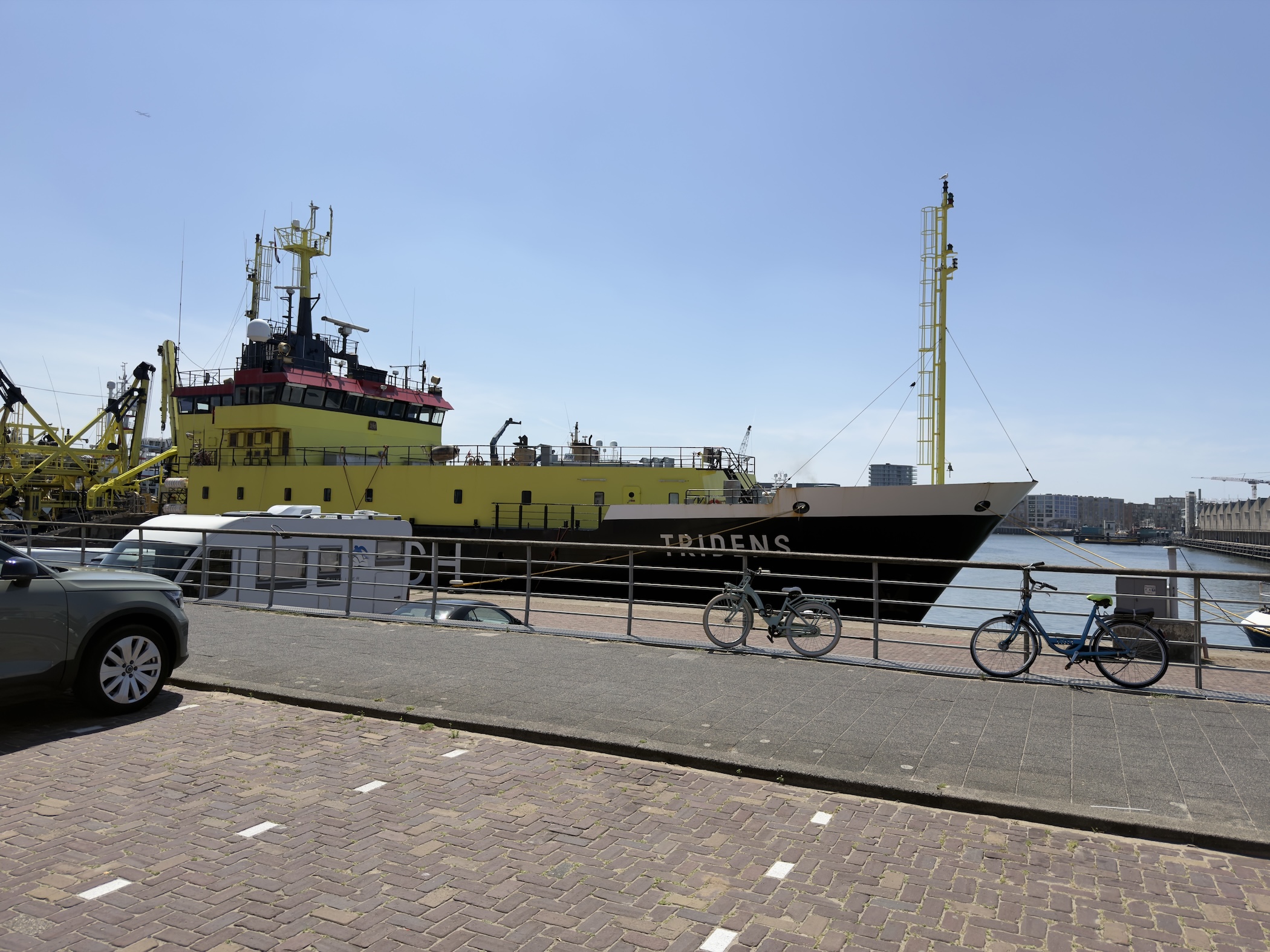 A yellow and black fisheries vessel named Tridens moored at a harbour quay with two bikes leaning on the railing.