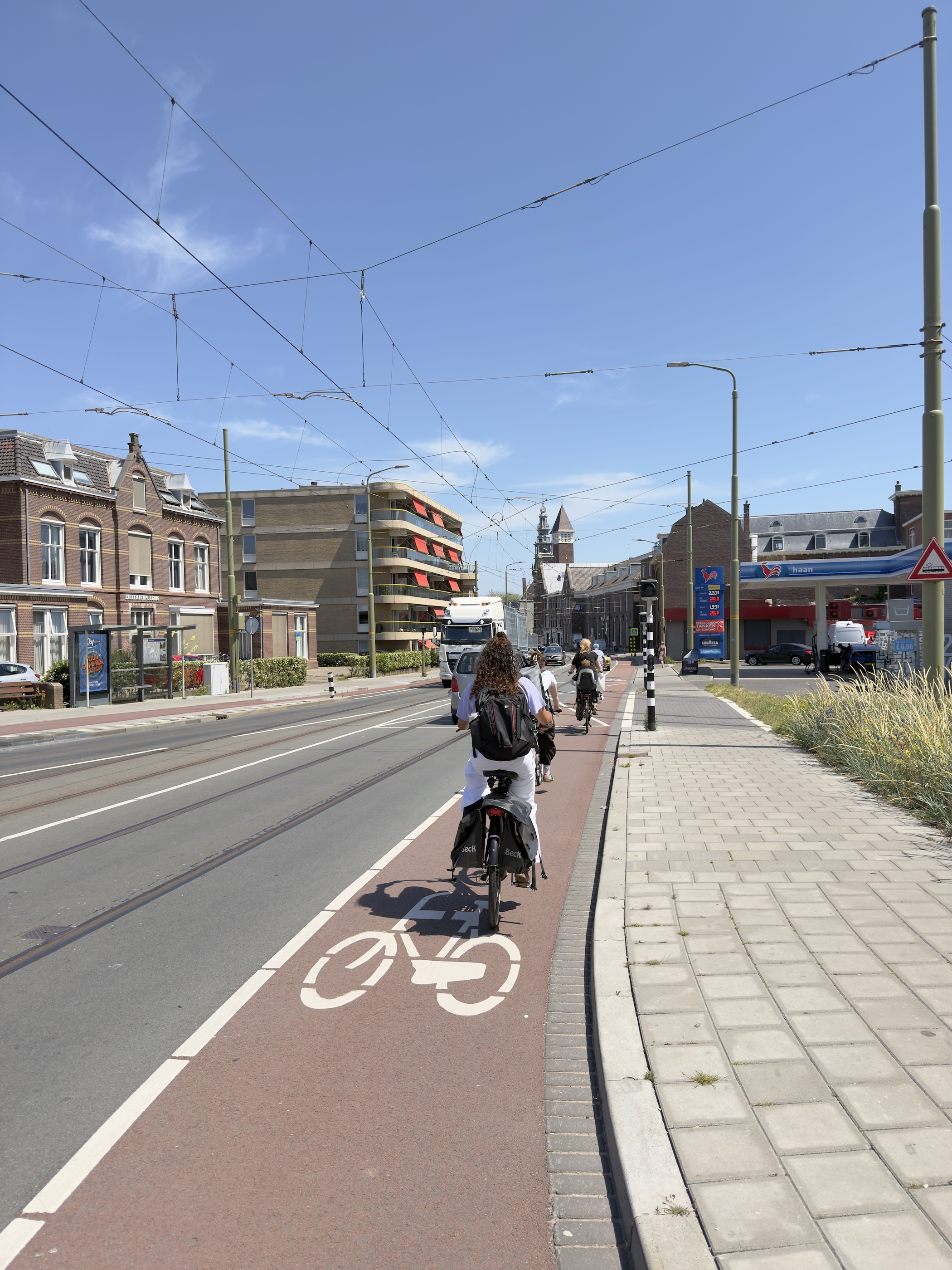 Cyclists riding a red cycle lane between tram tracks towards a distant church tower.