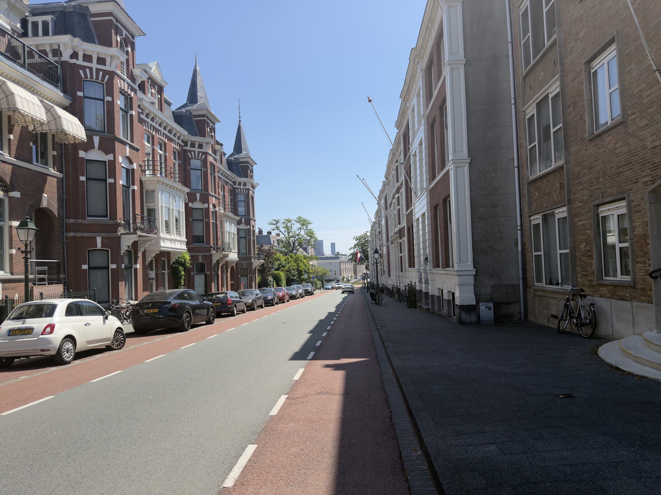 A quiet city street lined with grand brick townhouses and parked cars under bright sun.