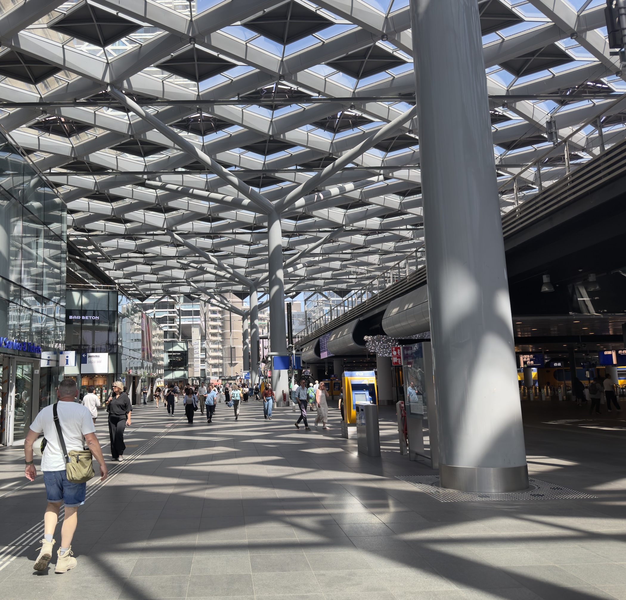 The diamond-patterned canopy of The Hague Central Station above commuters and platforms.