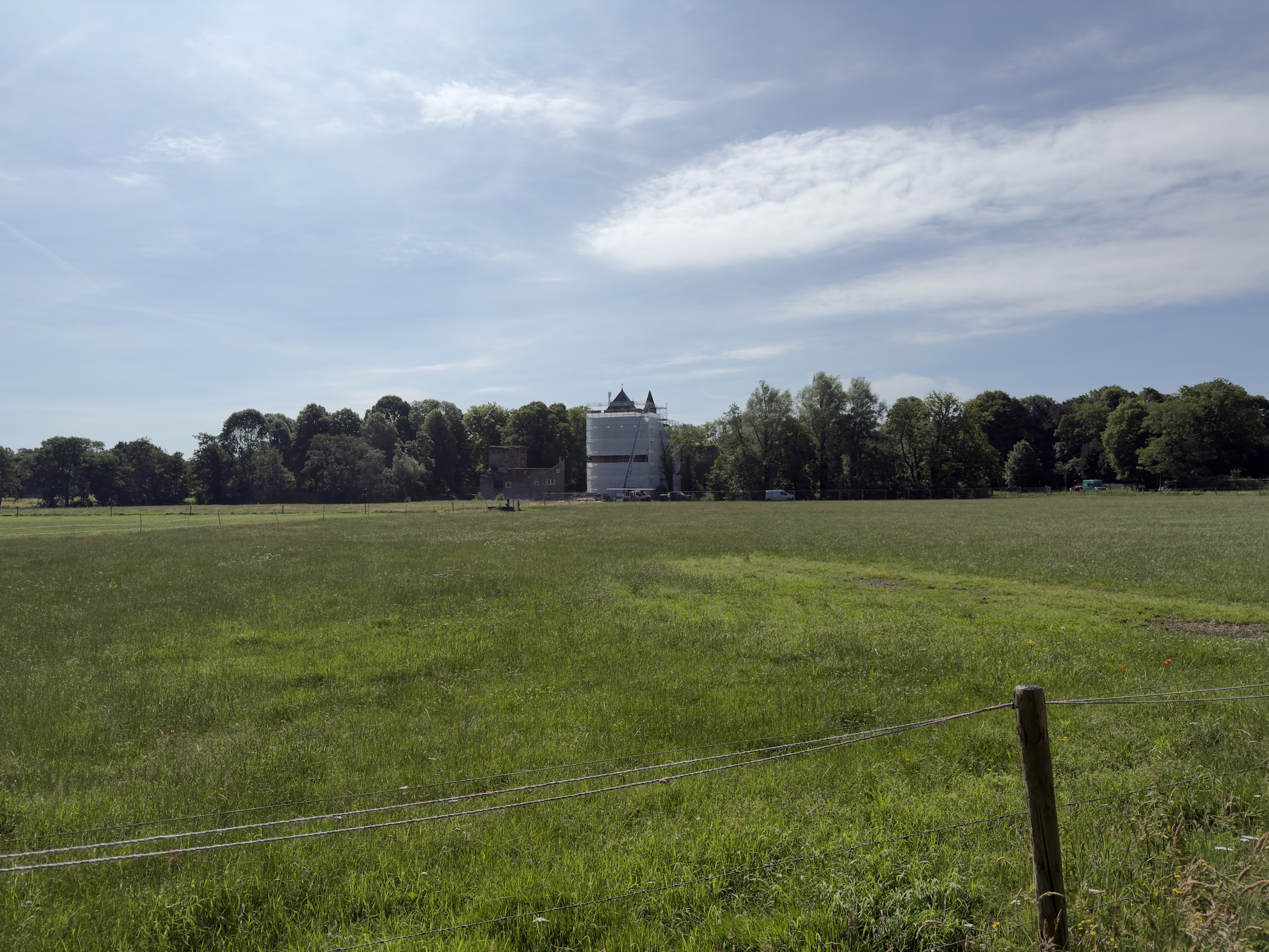 A white country house among trees beyond a fenced green meadow under a cloudy sky.
