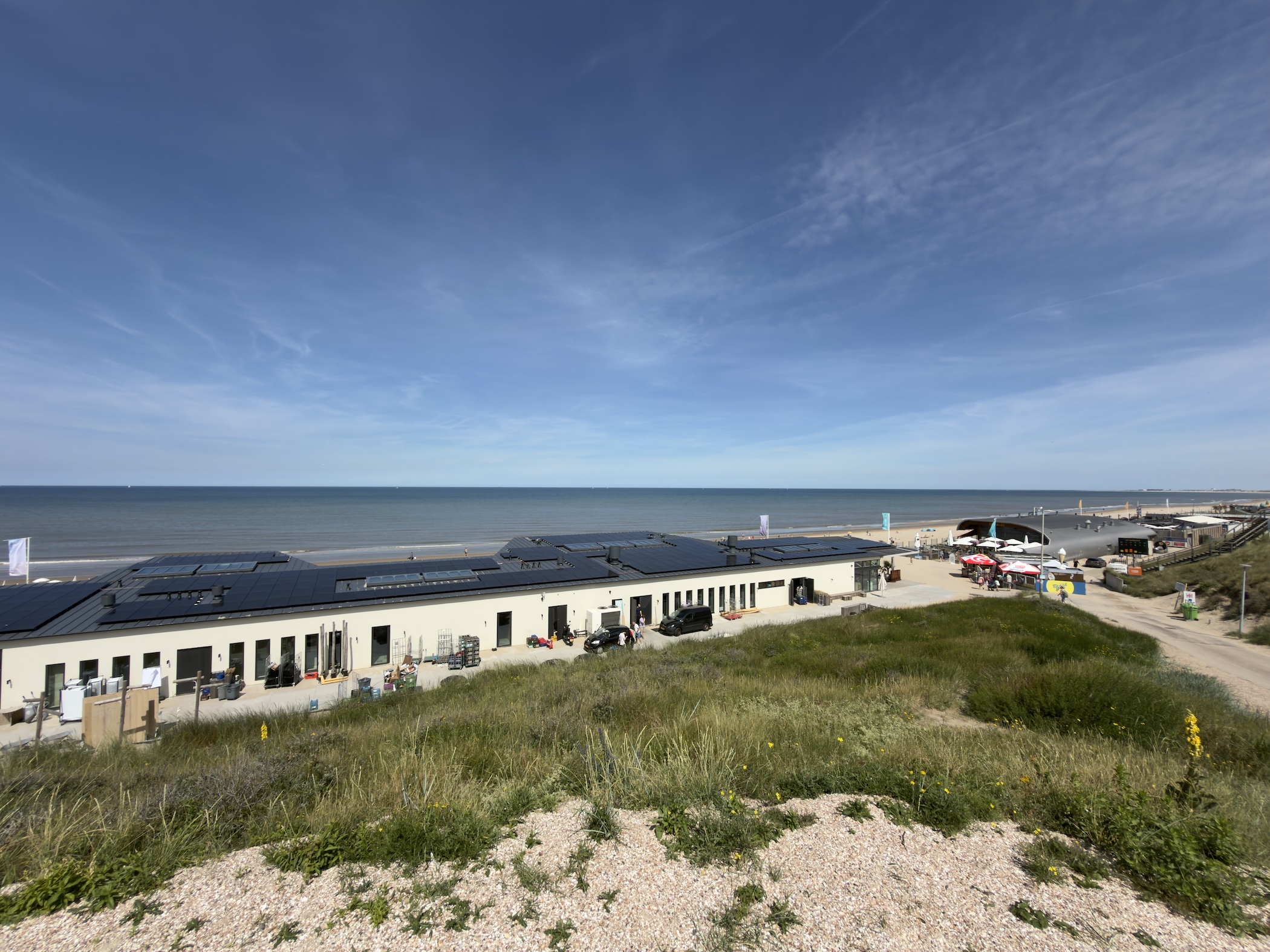 A low beach pavilion with solar panels overlooking the North Sea under a wide blue sky.