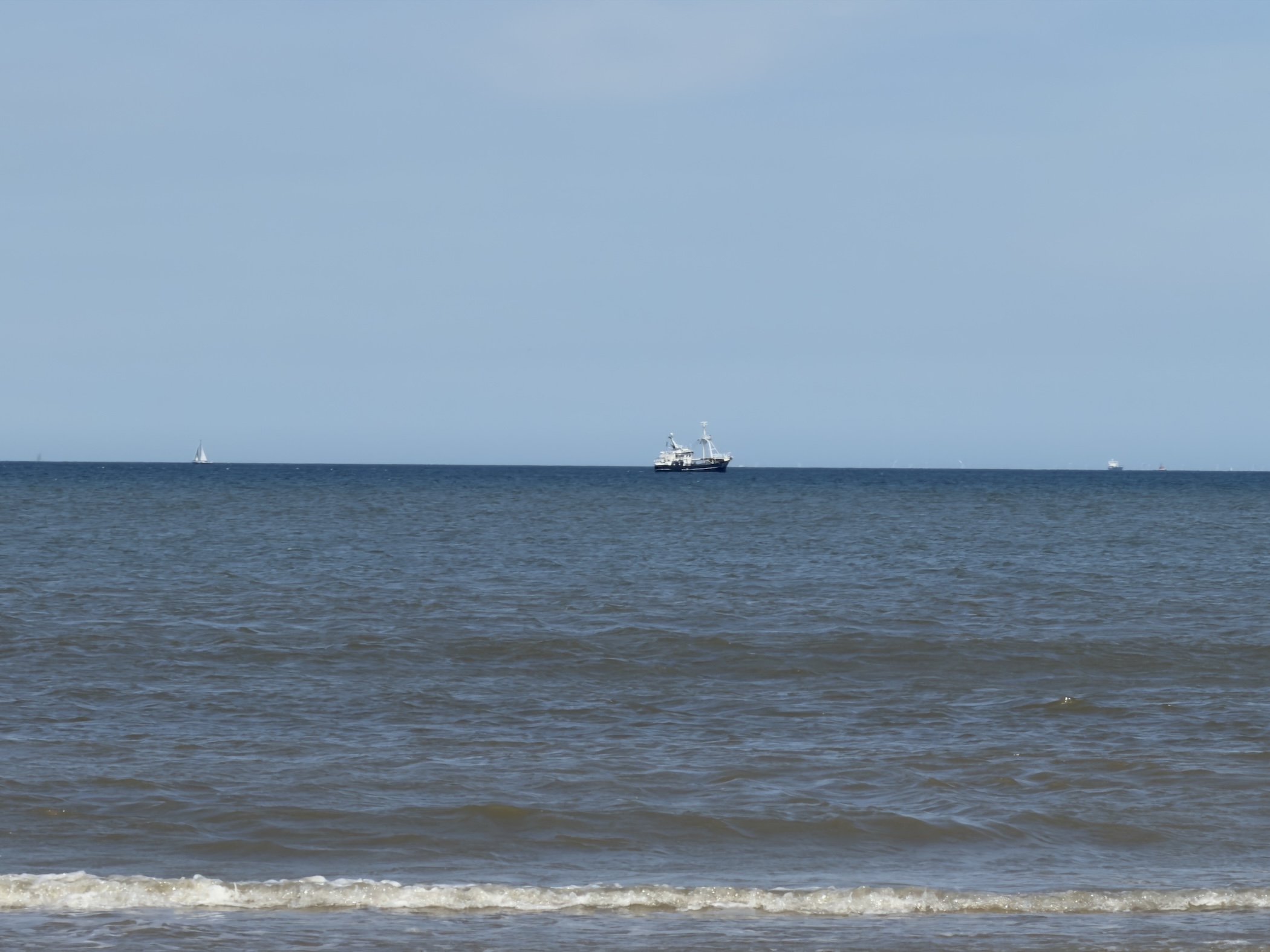 A fishing trawler and a distant sailing boat on the calm North Sea horizon.