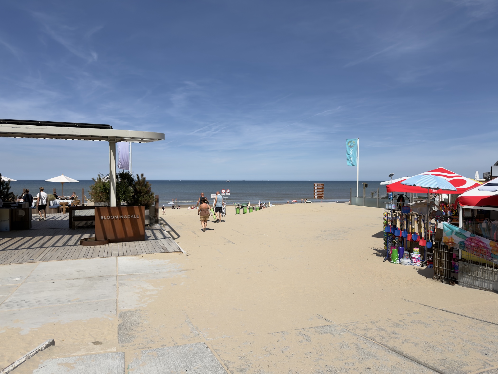 A beach entrance with a seaside terrace, parasols and a colourful kiosk.