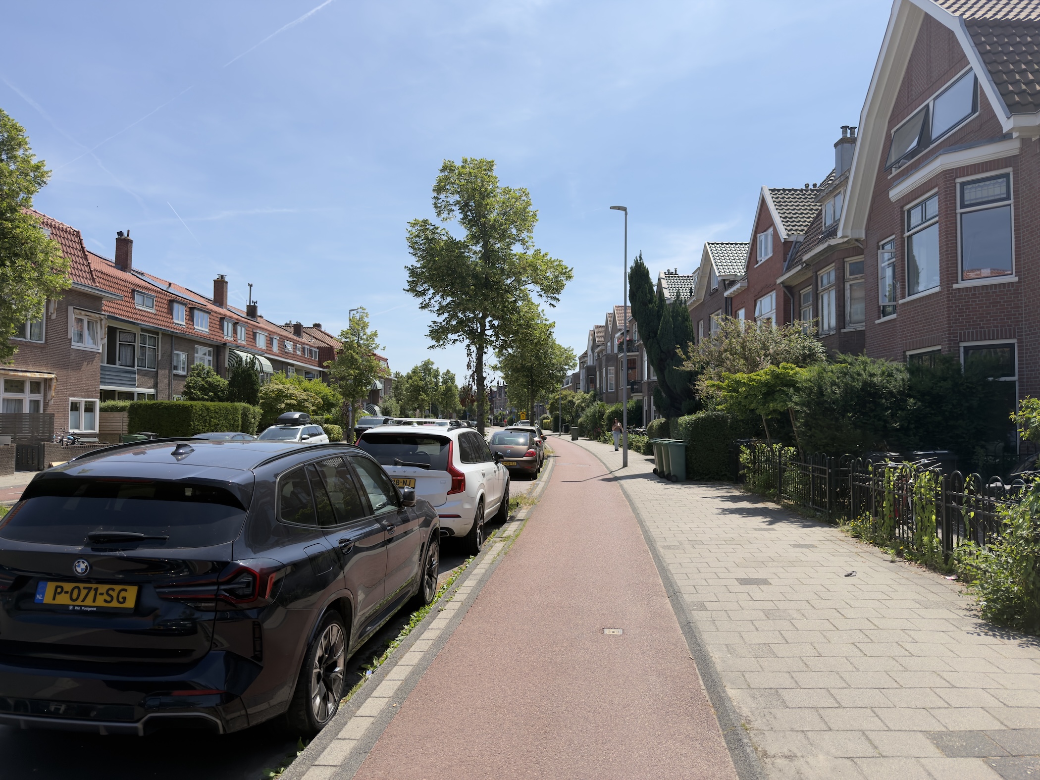 A residential street with parked cars, brick houses and a red-paved cycle lane.