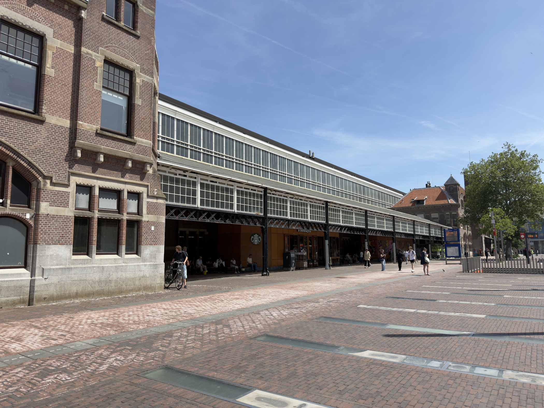 A long glass-roofed market hall of brick and steel beside a wide paved square.