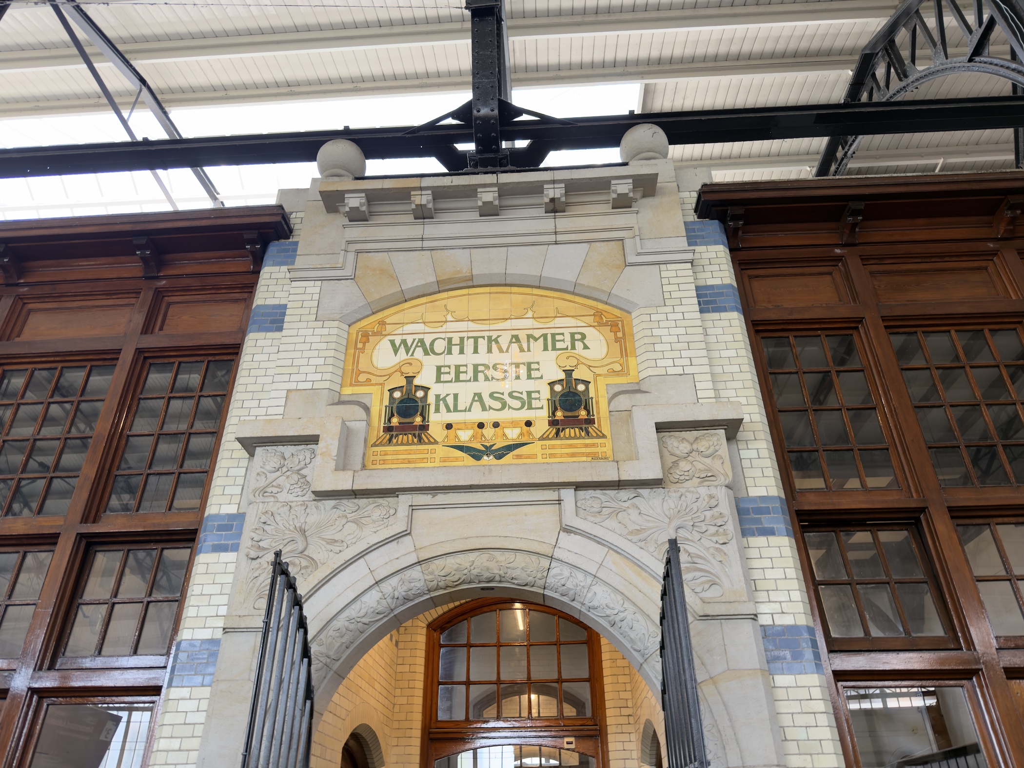 An ornate tiled station panel lettered Wachtkamer Eerste Klasse above an arched doorway.