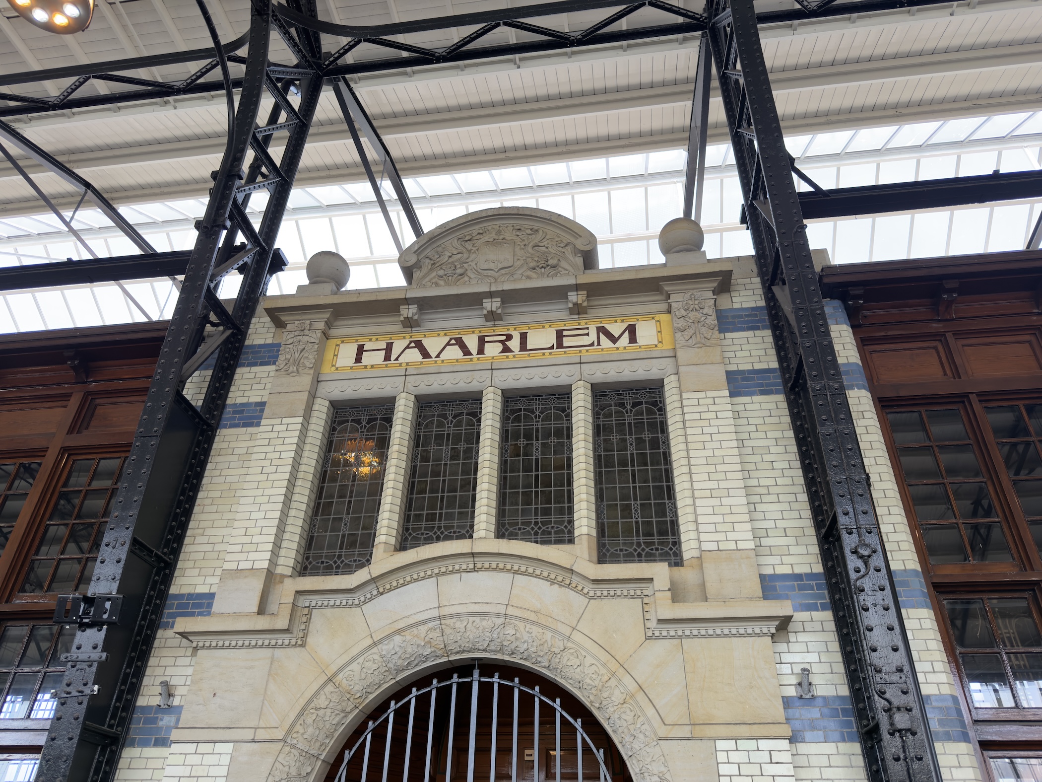 A tiled and steel station interior with a gold panel lettered Haarlem above arched windows.