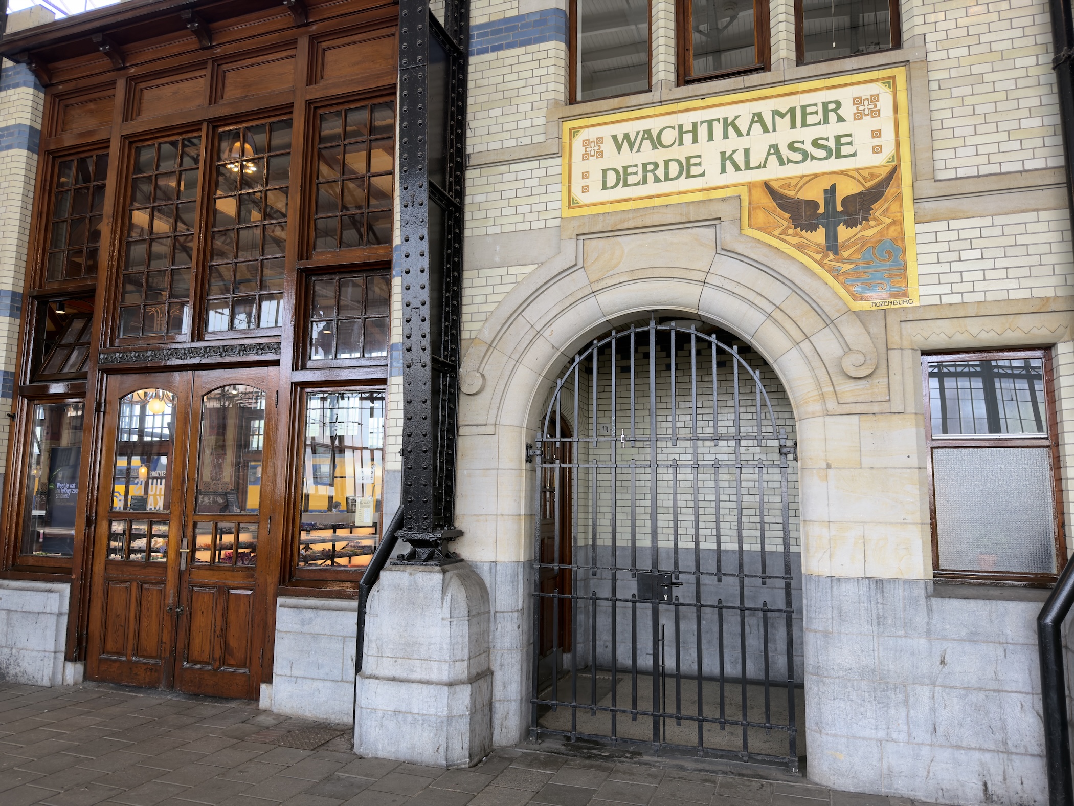 A station wall with wooden doors and a tiled panel lettered Wachtkamer Derde Klasse.