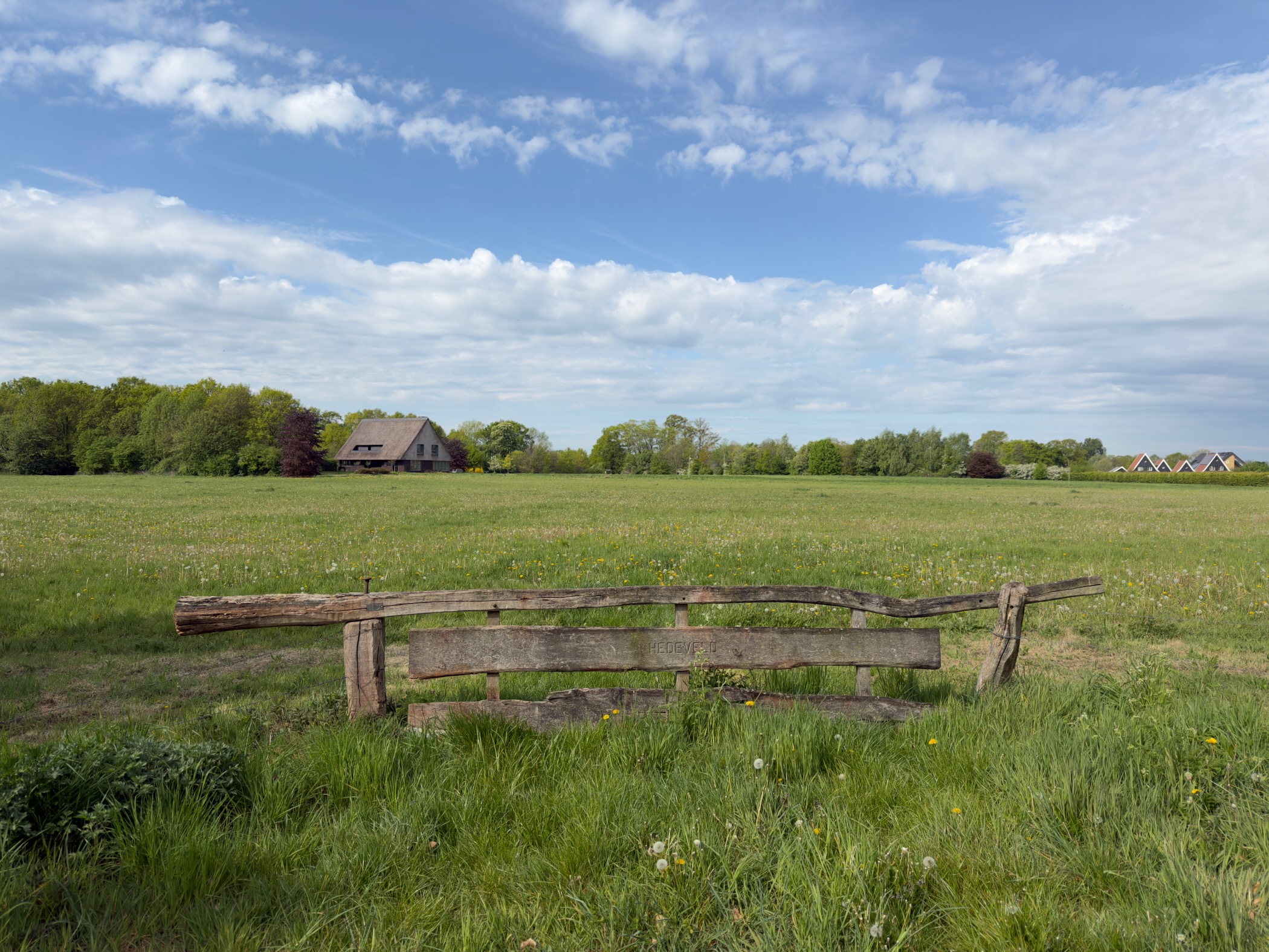Old wooden fence in a meadow with a traditional Dutch farmhouse in the distance