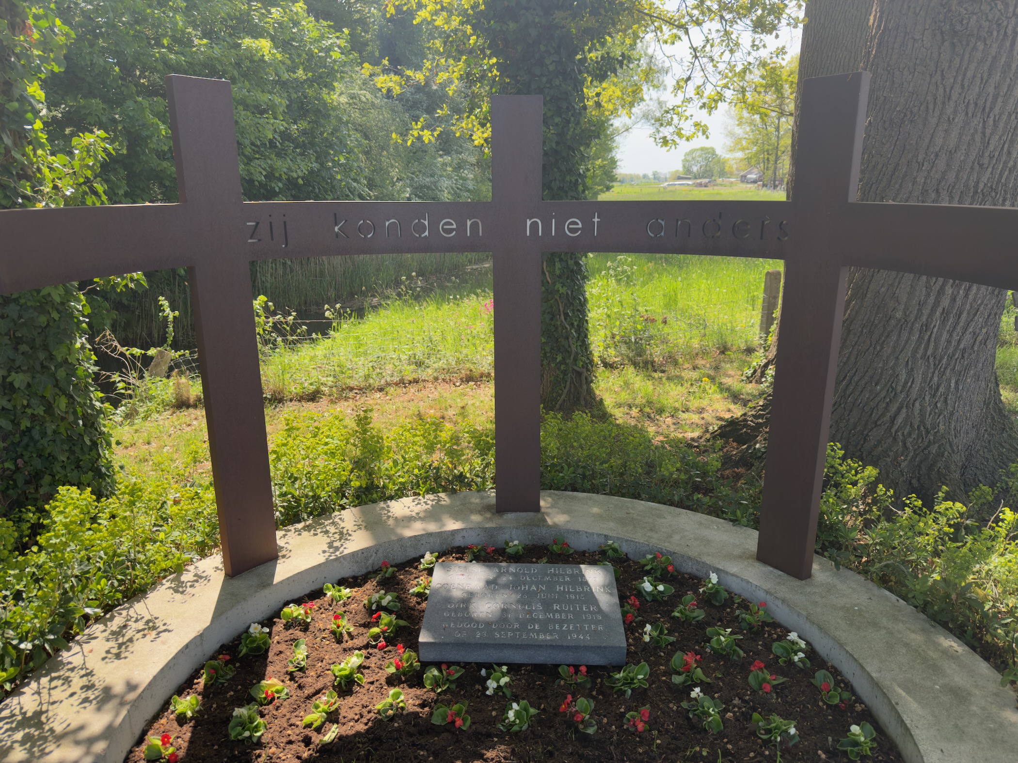 Memorial with three iron crosses and an engraved stone surrounded by red flowers