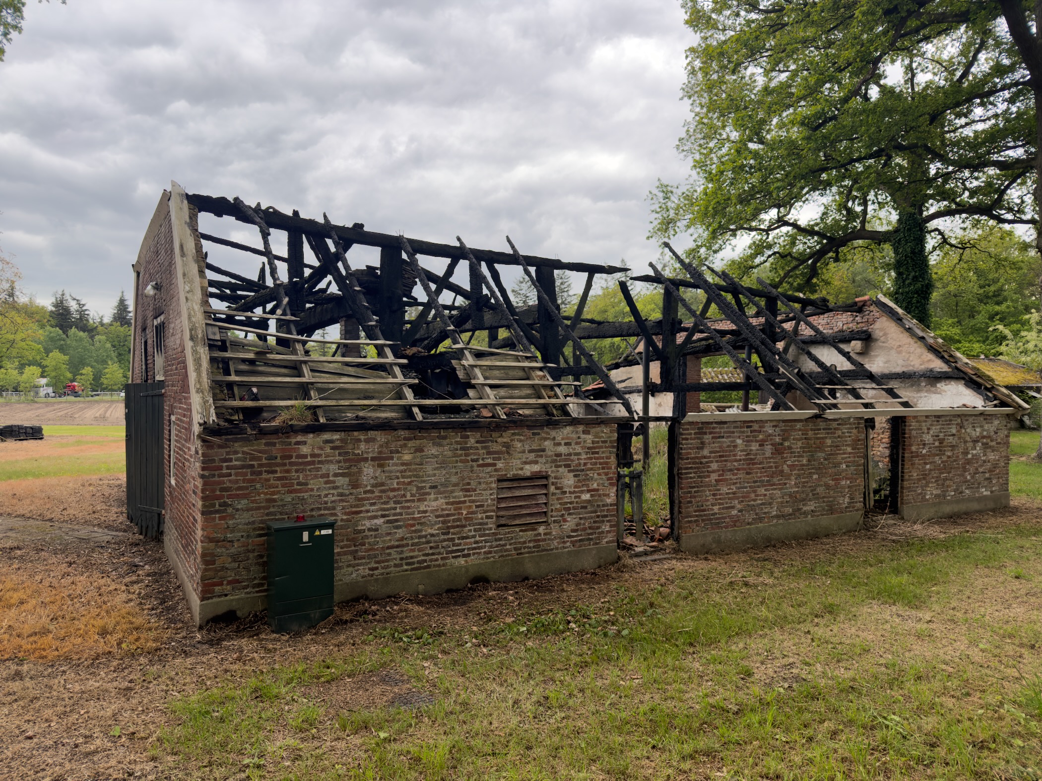 Burnt-out brick barn with charred roof timbers exposed against an overcast sky