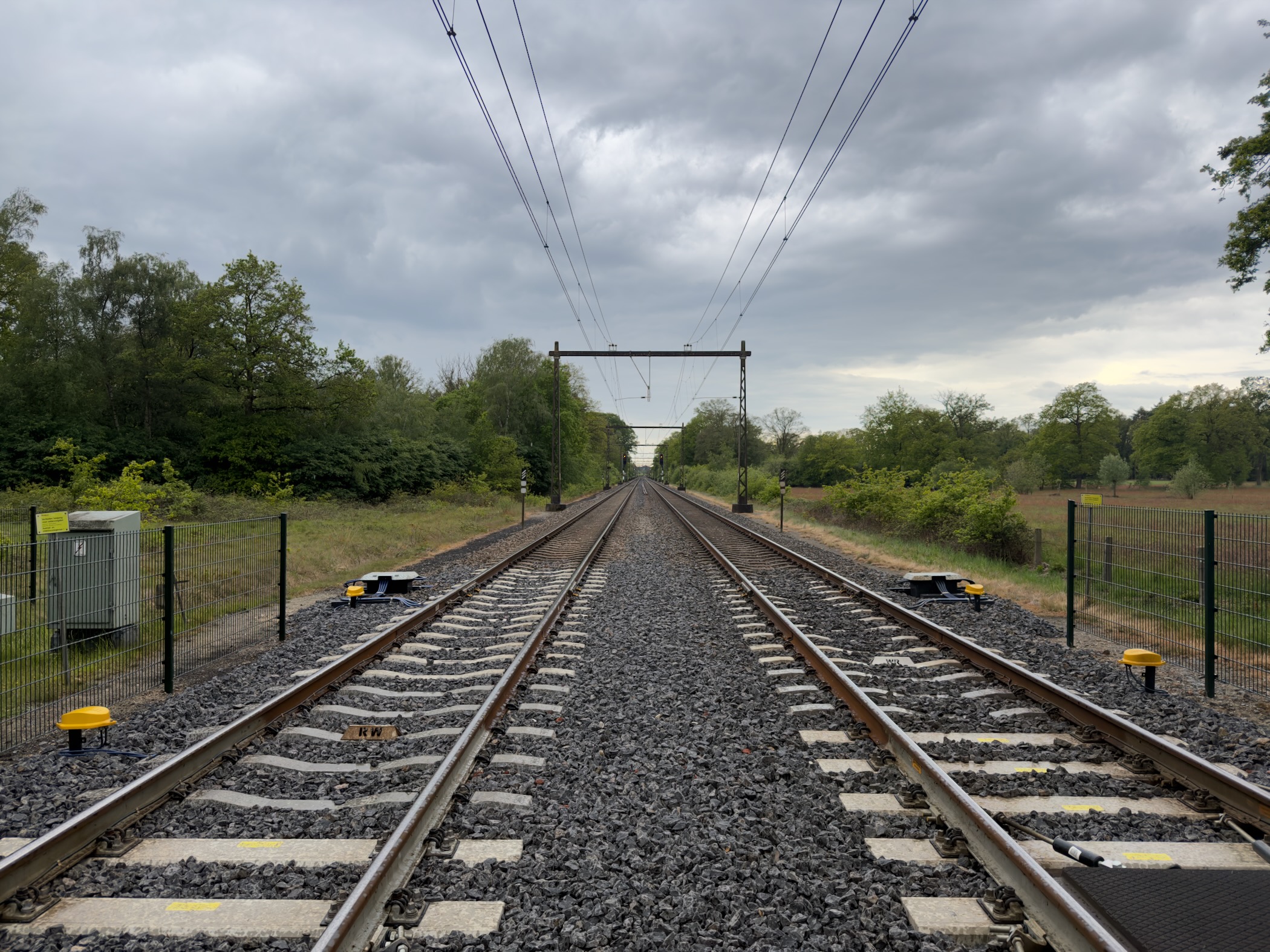 View down a straight stretch of railway track with overhead lines disappearing toward the horizon