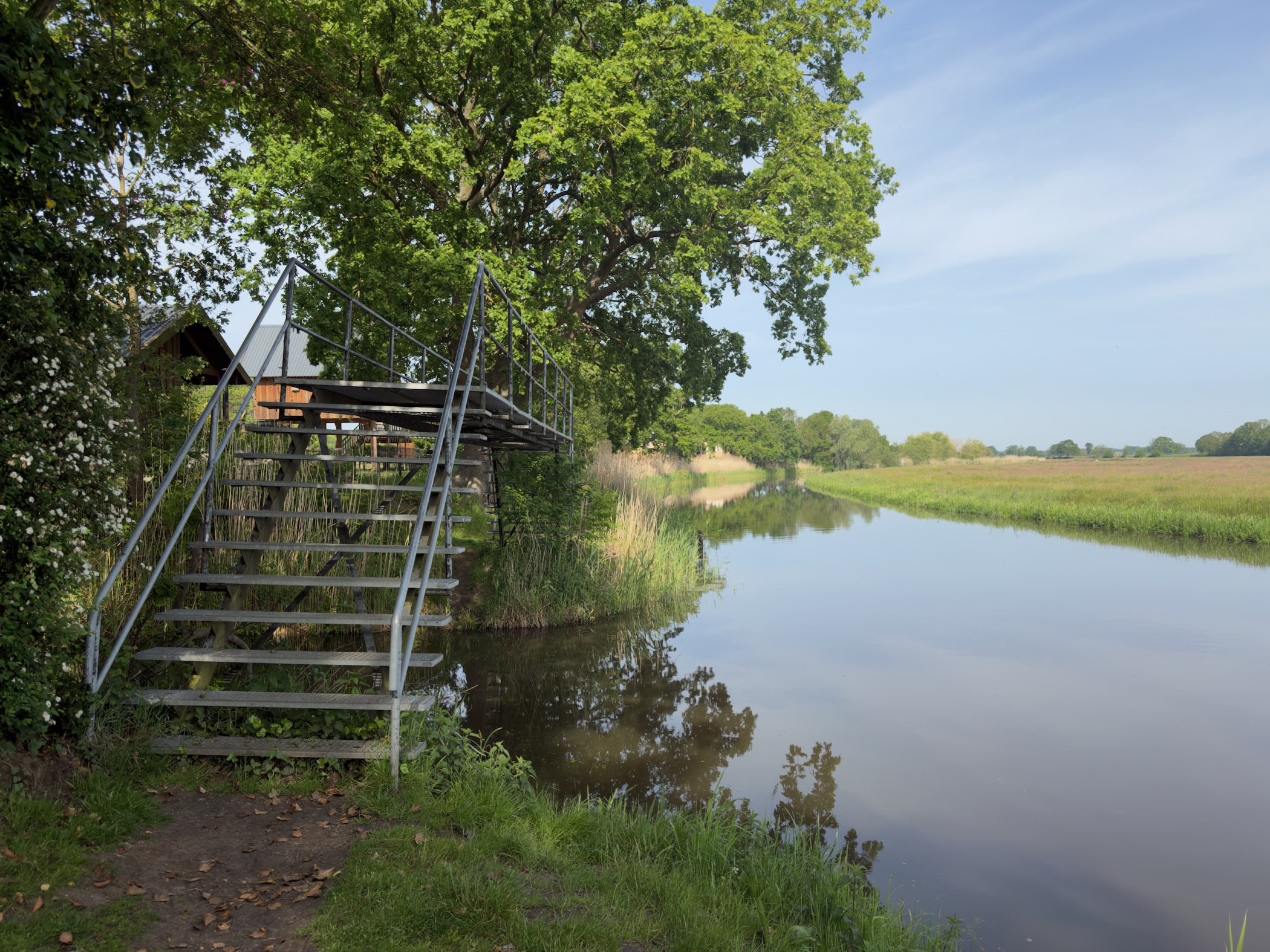 Wooden viewing platform with a metal staircase beside a reed-lined stretch of the Regge