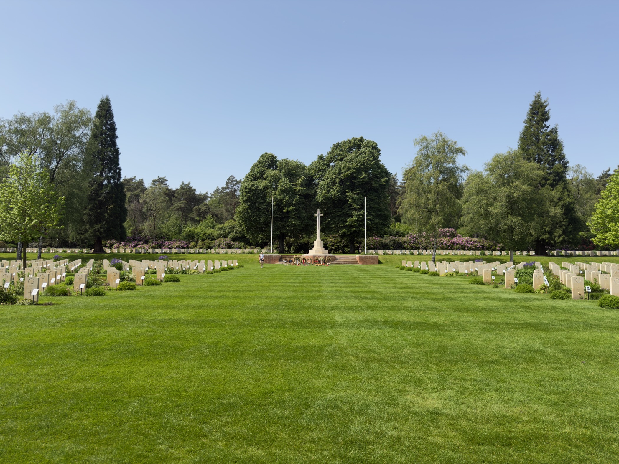 Long view across the Canadian War Cemetery with rows of white headstones flanking the Cross of Sacrifice