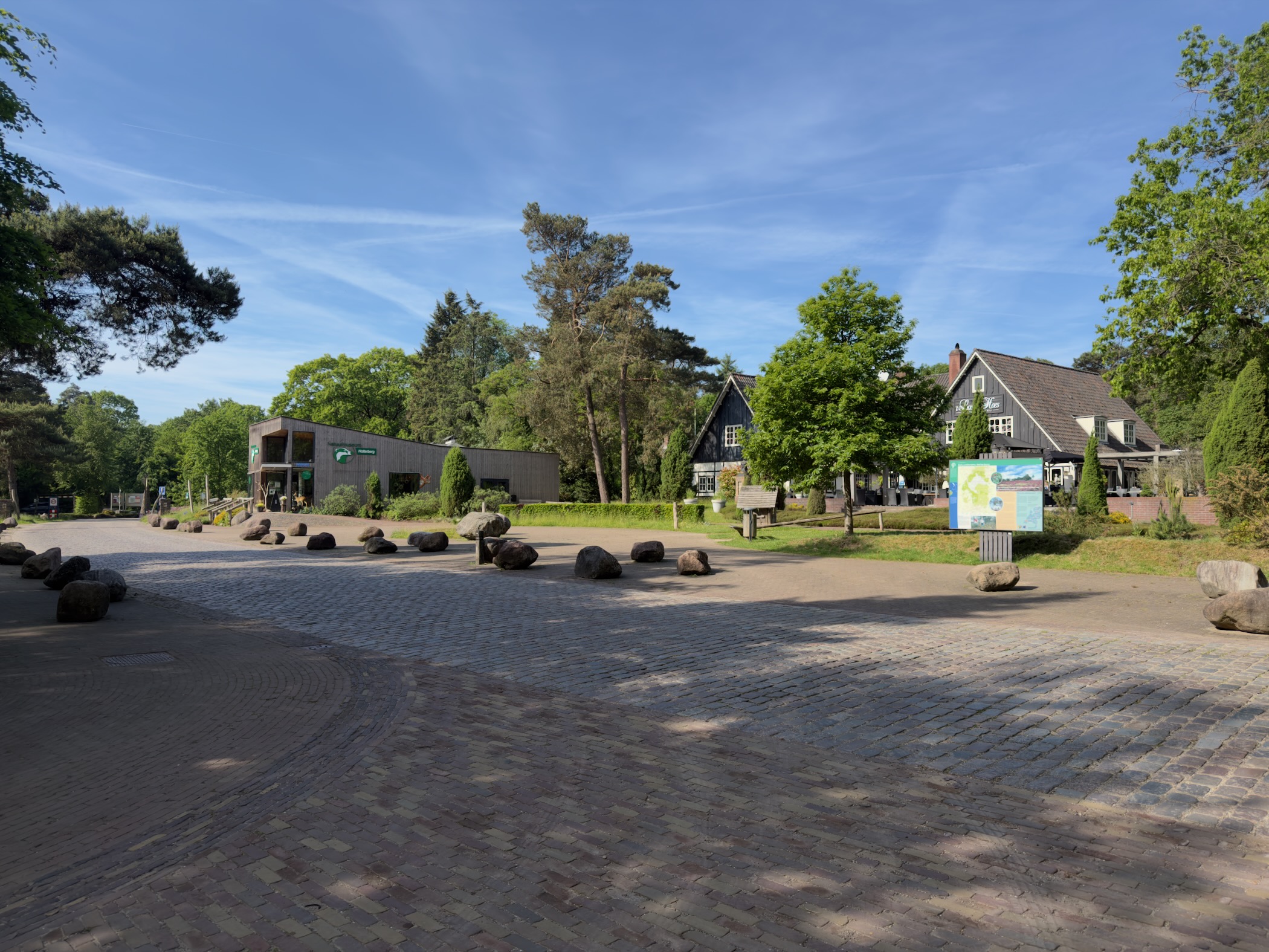 Paved forecourt at the Holterberg visitor centre with boulders and an information board