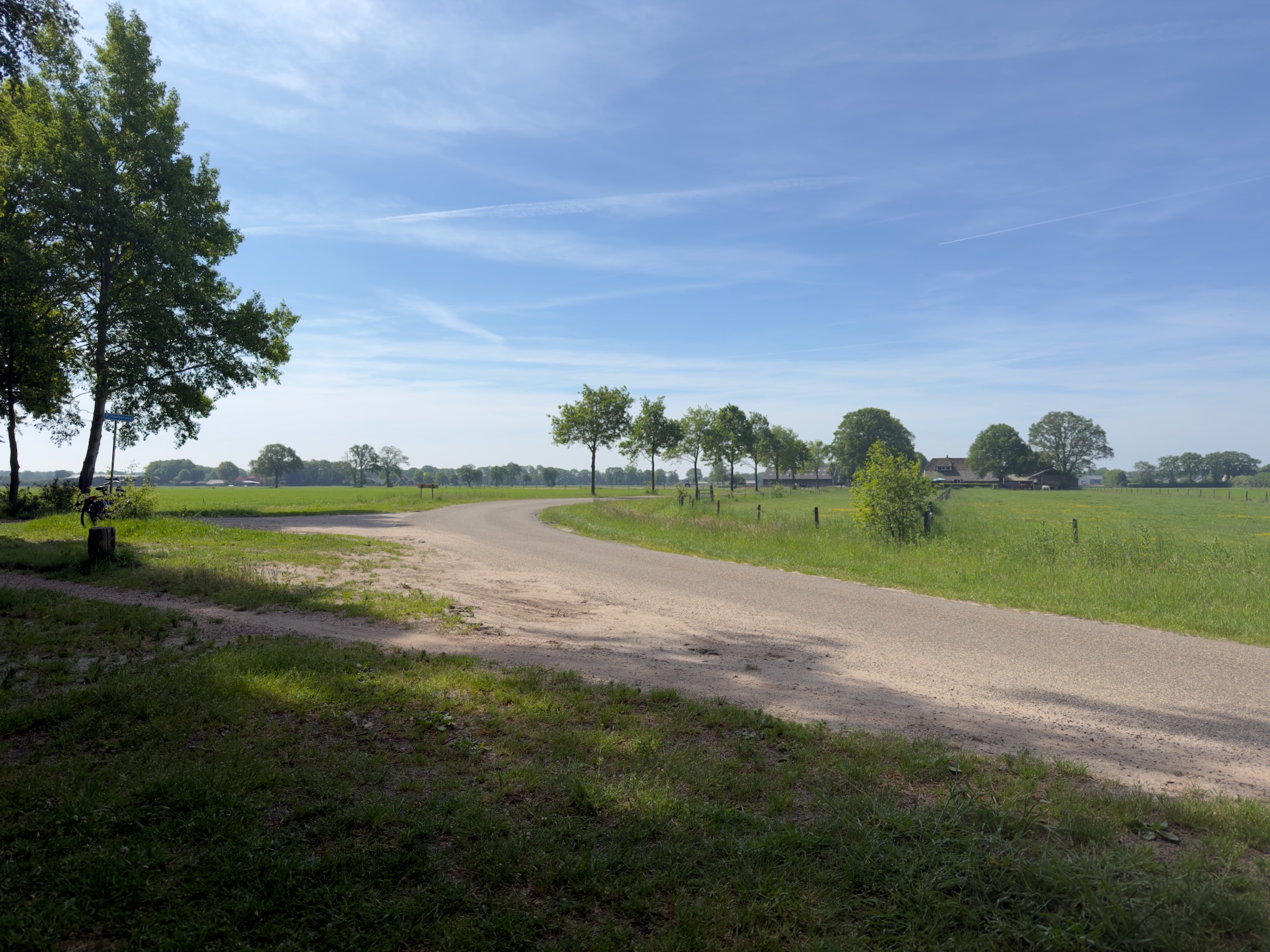 Junction of quiet country lanes between flat farmland and scattered trees