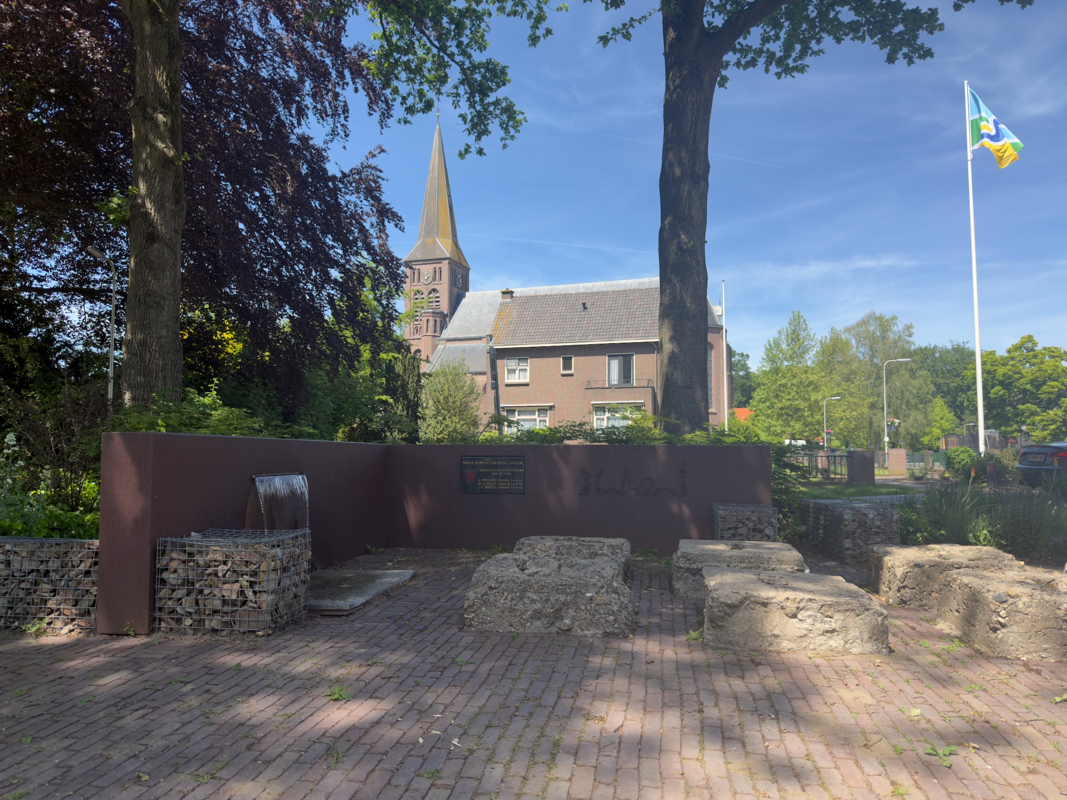 Small village square in Lettele with a low stone monument in front of the parish church
