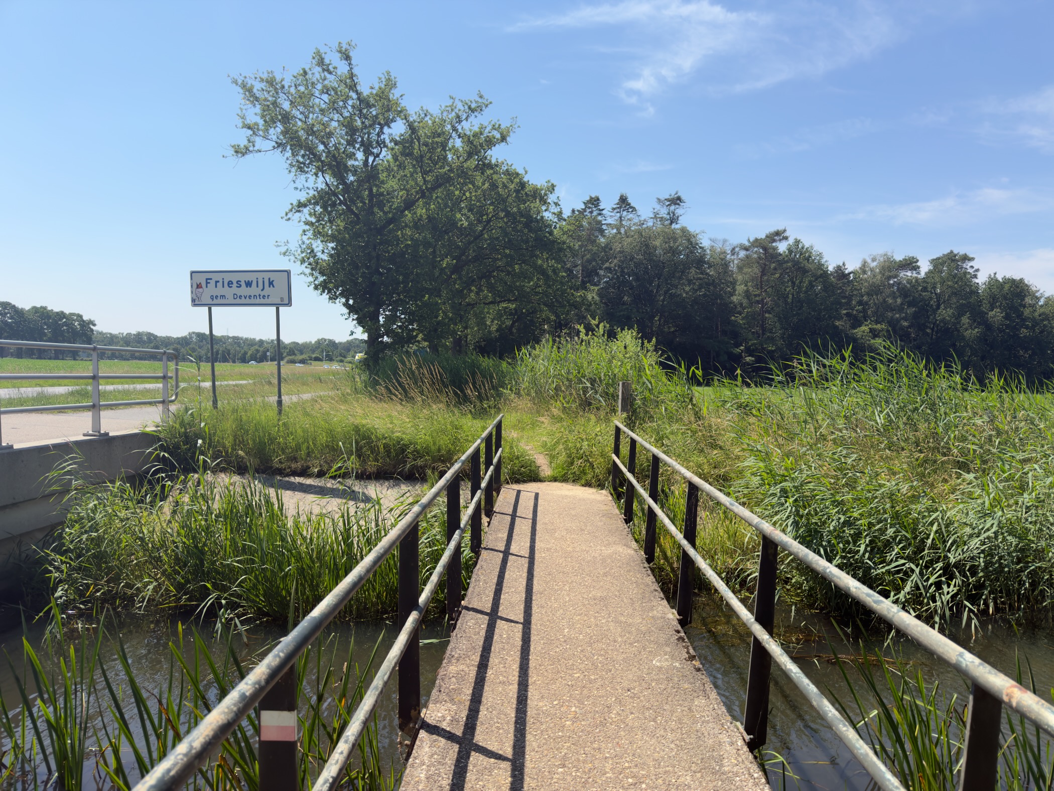 A concrete footbridge with railings crossing a ditch, with a Frieswijk place-name sign beyond.
