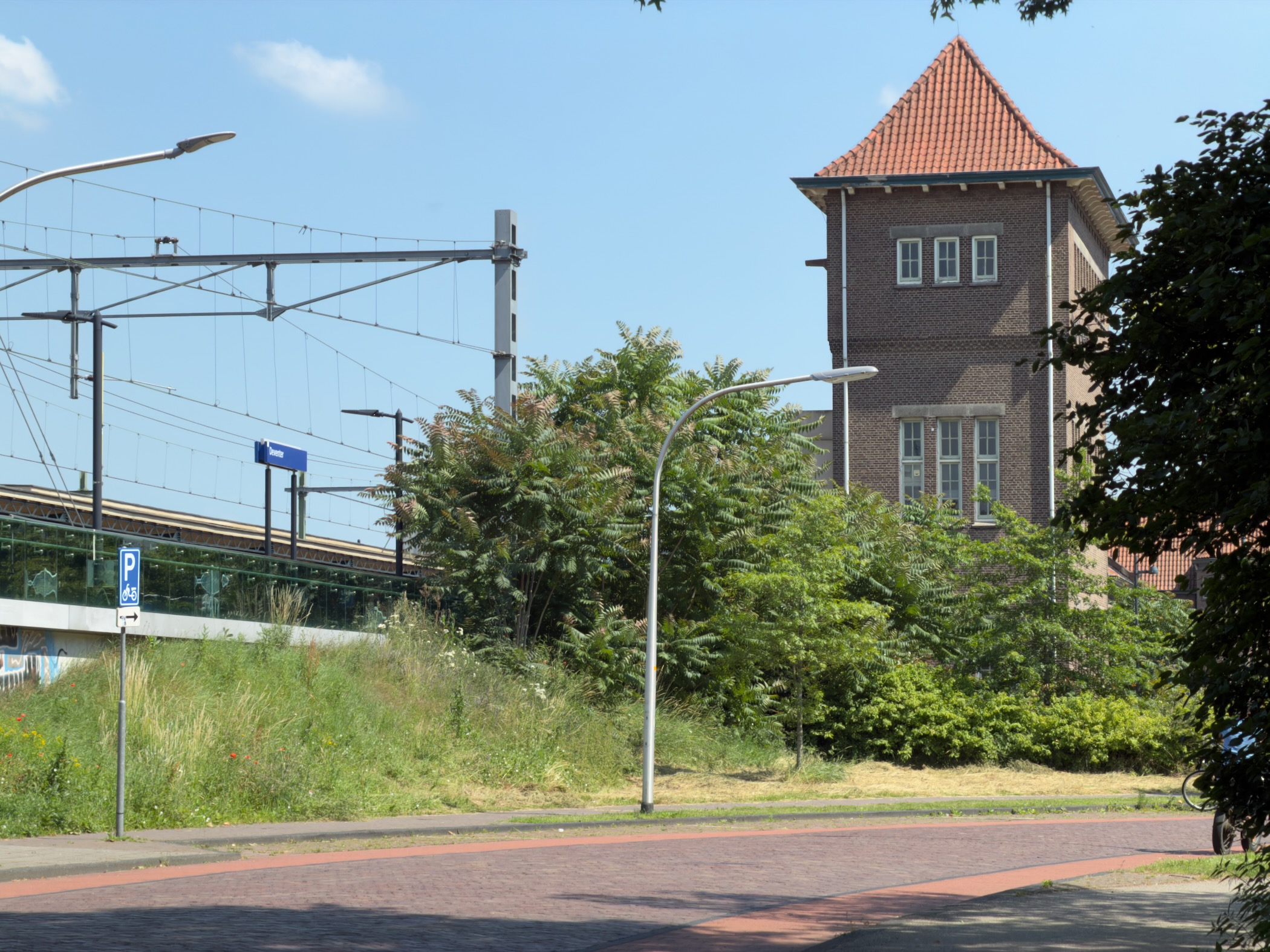 Deventer station with overhead railway lines and a tall brick water tower behind.