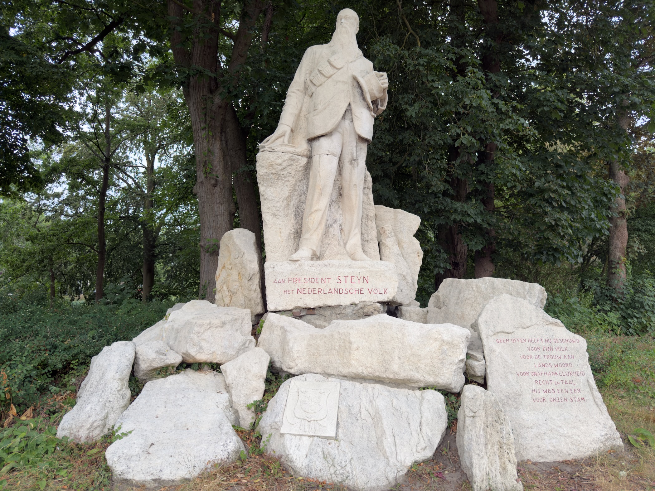 A white stone statue of President Steyn among pale rocks, dedicated by the Dutch people and set among trees.