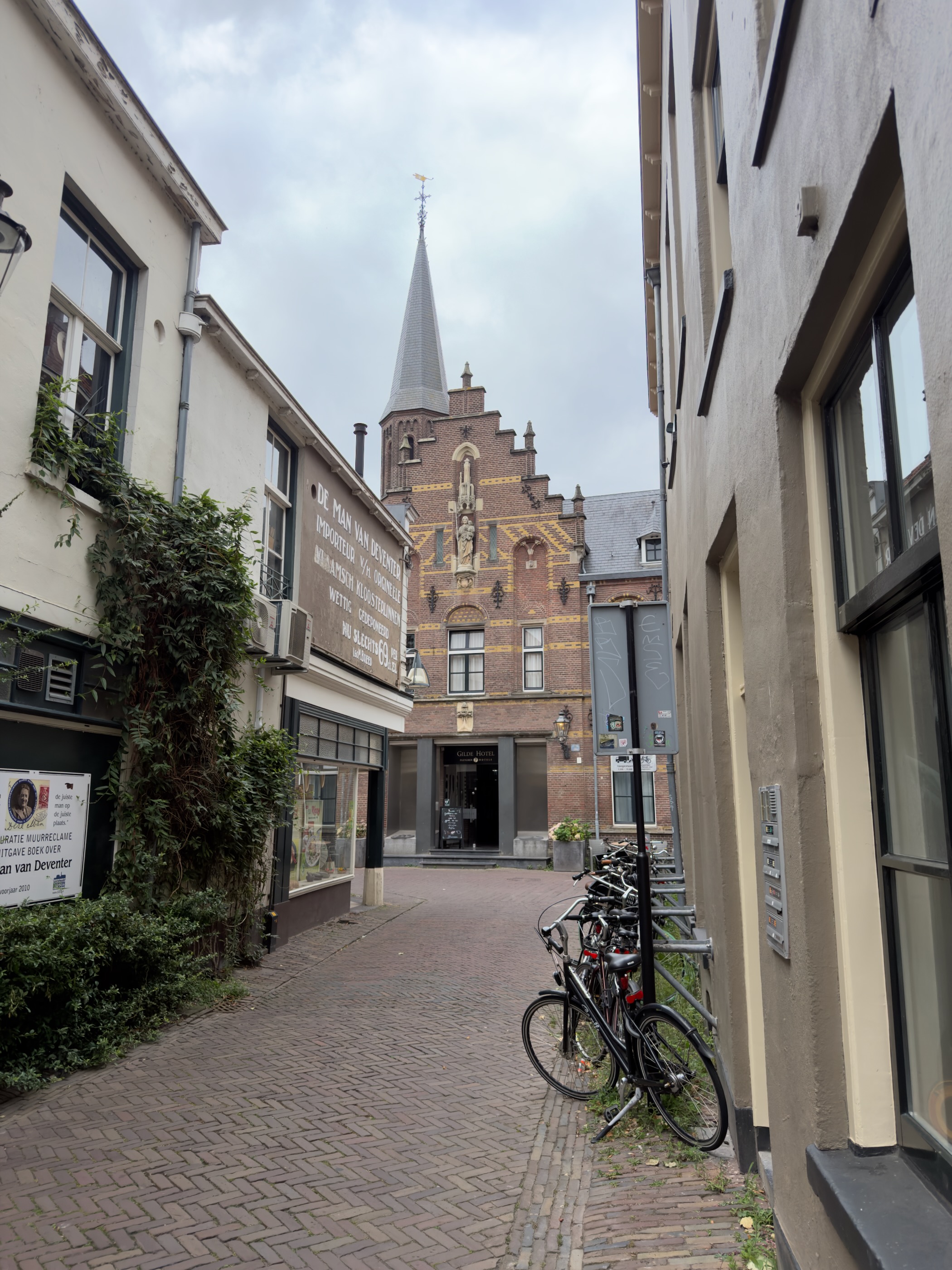 A narrow Deventer alley of brick paving with parked bicycles, leading to a stepped brick gable and church spire.