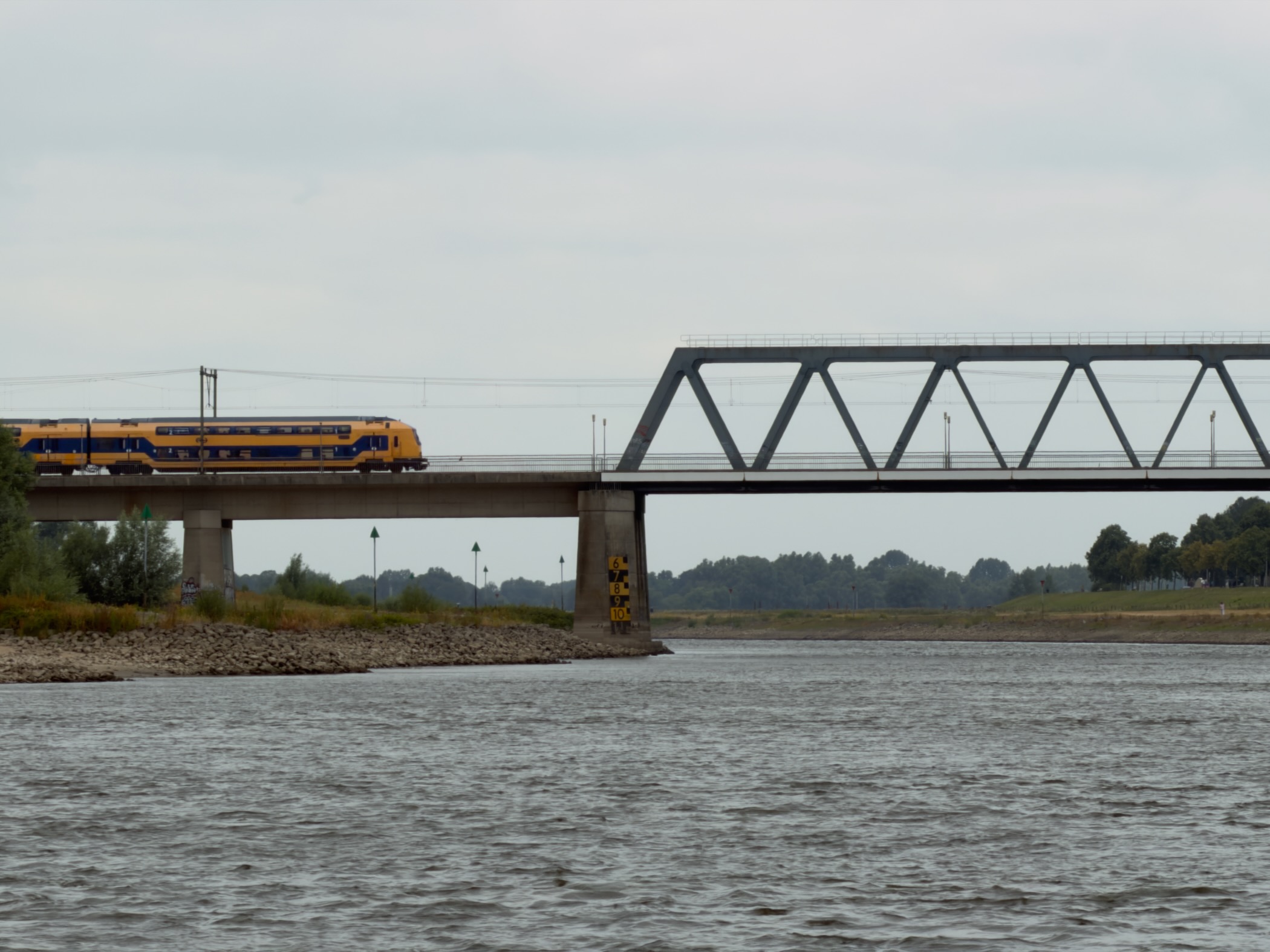 A yellow and blue double-decker train crossing a steel railway bridge over the IJssel.
