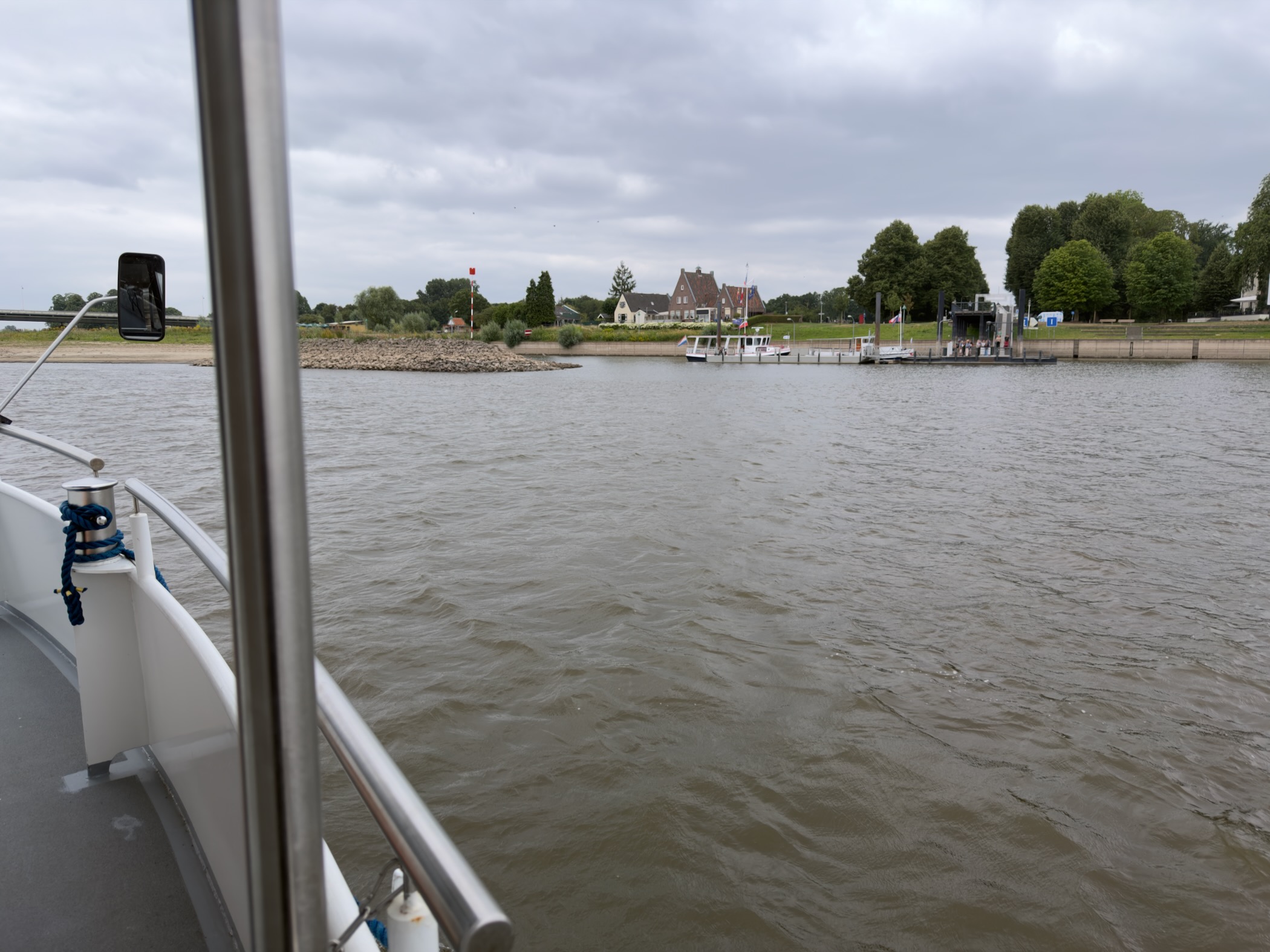 View from the ferry deck across the IJssel towards the opposite bank, jetty and houses under cloud.