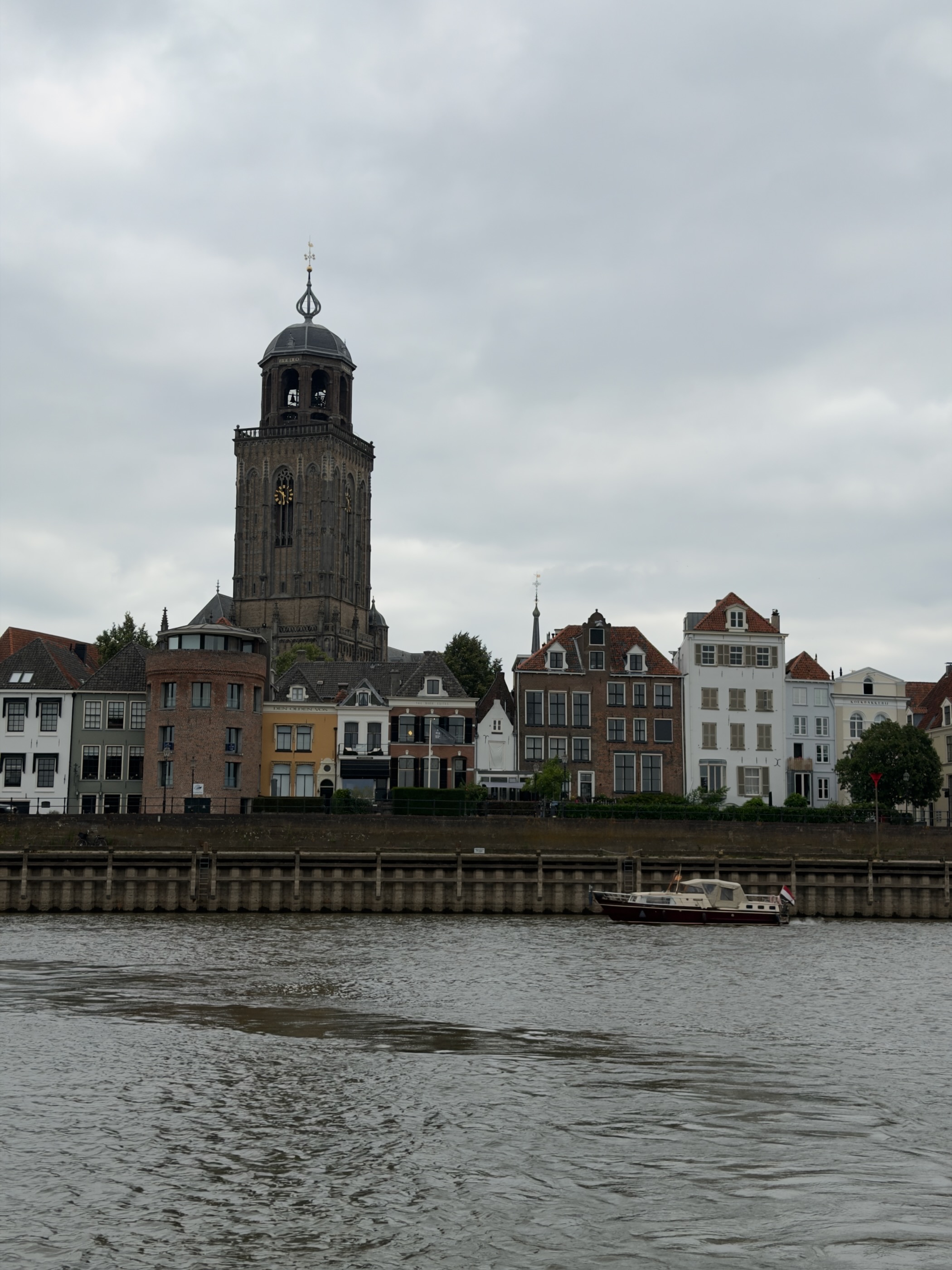 The Deventer waterfront with the Lebuinuskerk tower and colourful canal houses, a motorboat on the IJssel.