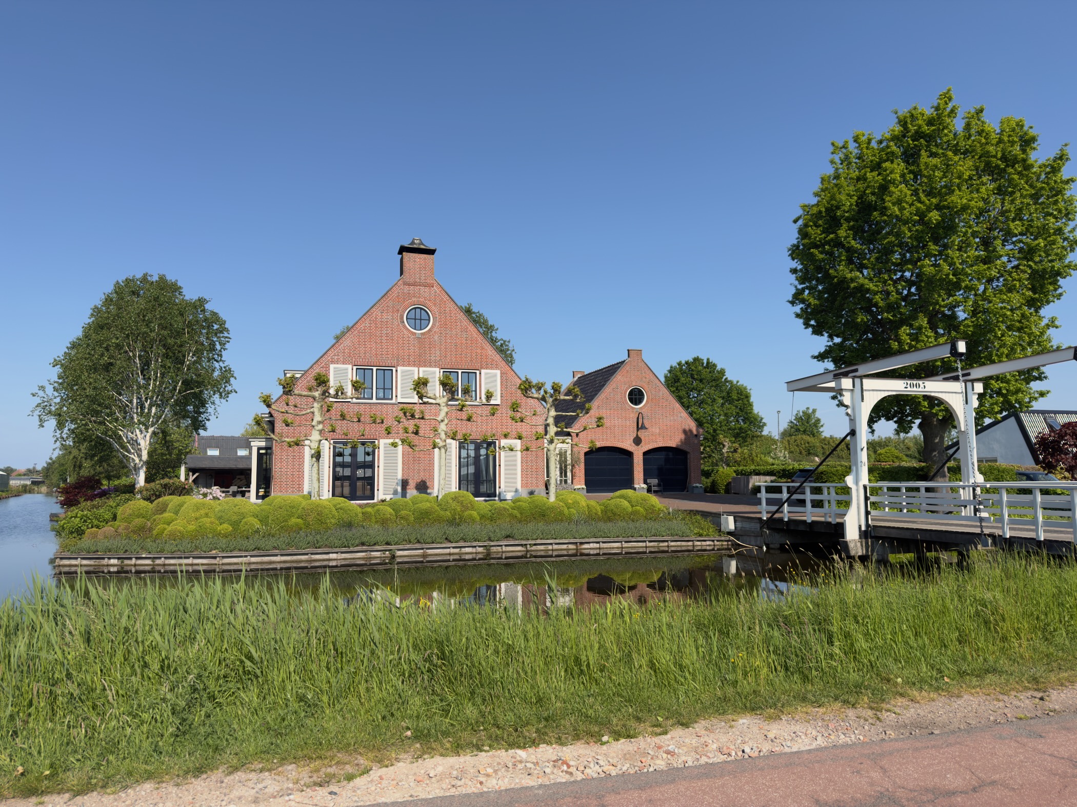 Brick farmhouse with a stepped gable beside a canal and small white drawbridge