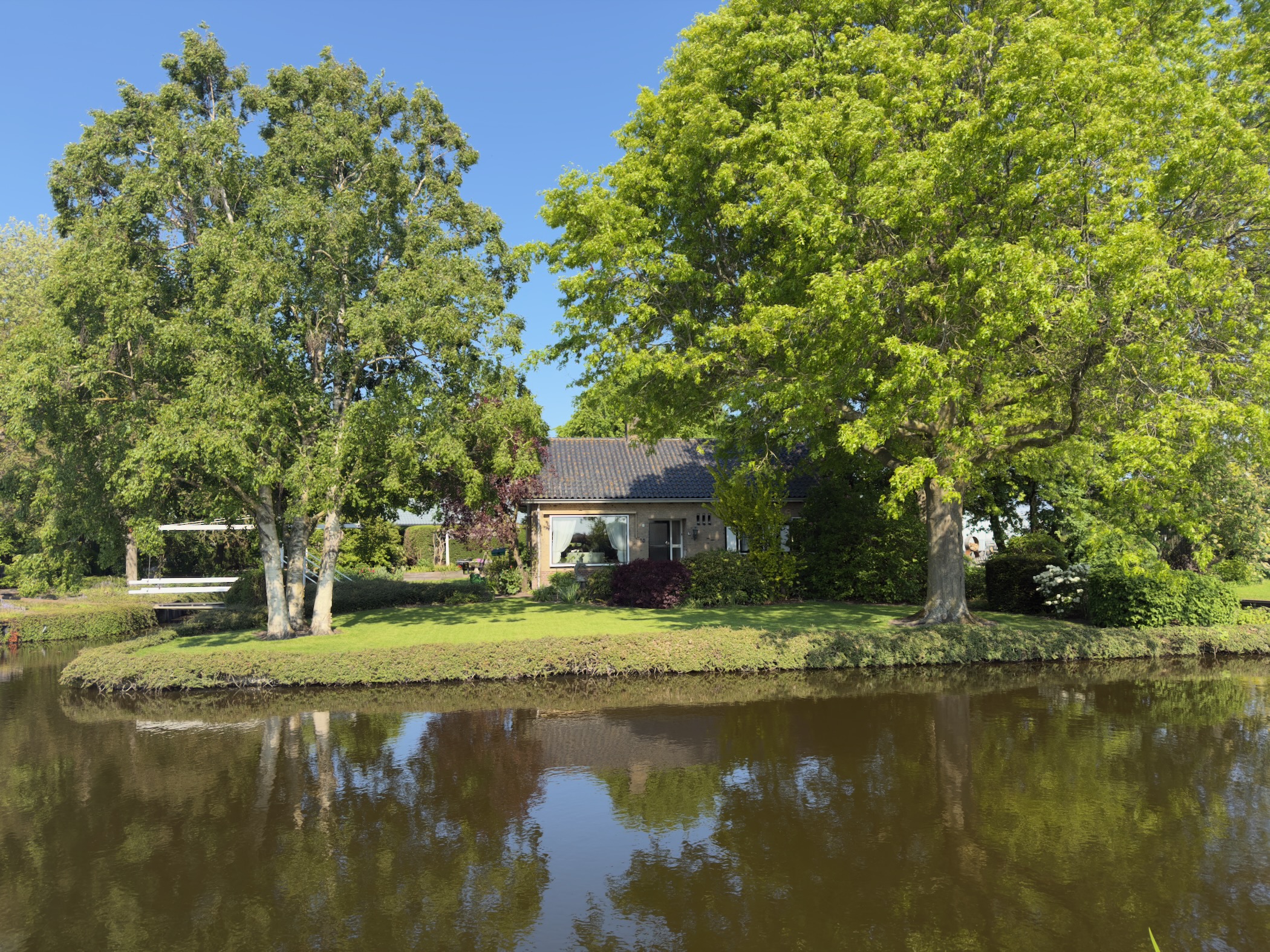 House framed by tall trees, mirrored in the still water of a canal