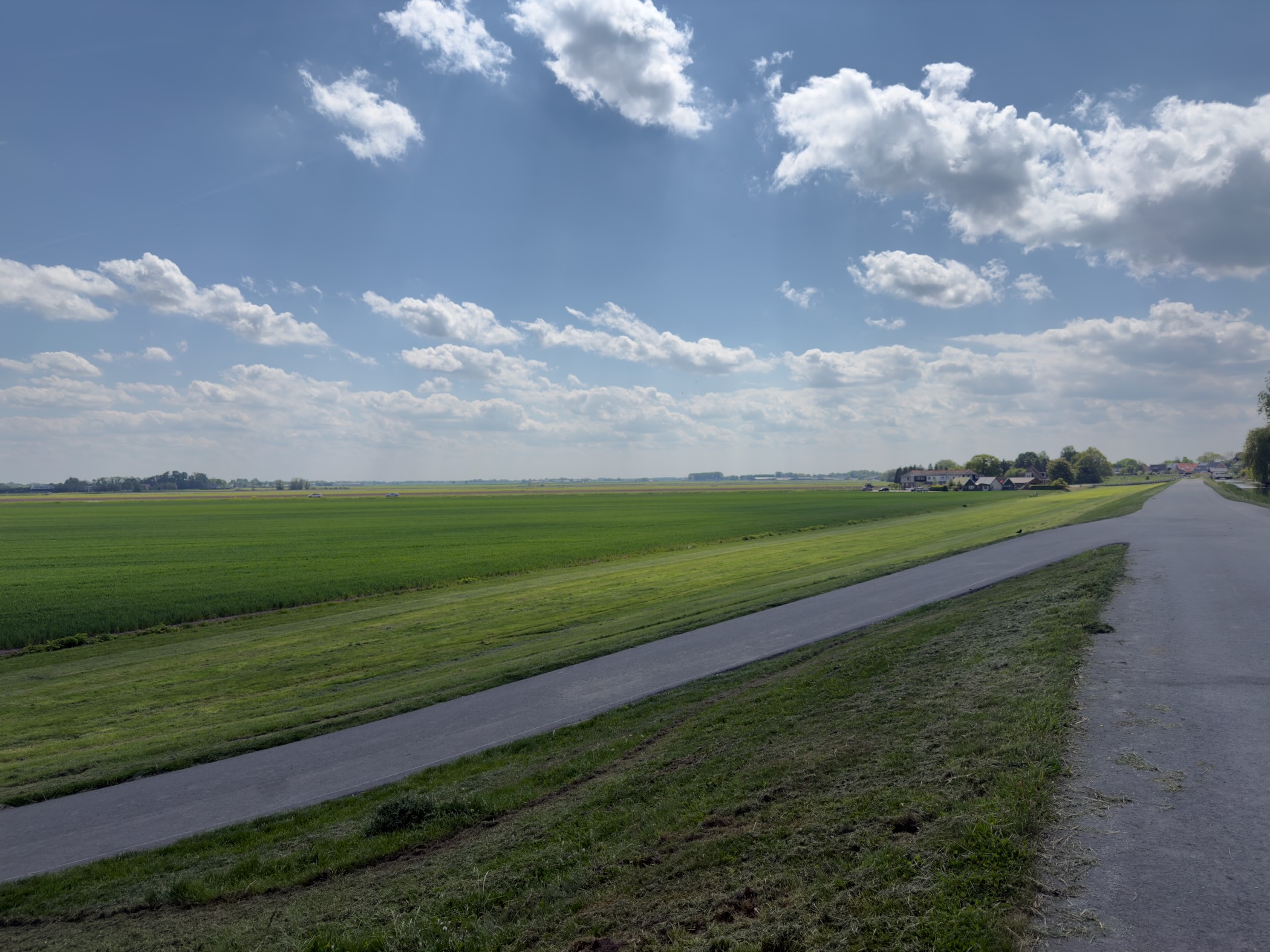 Long paved cycle path running through wide-open polder under a big cloud-streaked sky