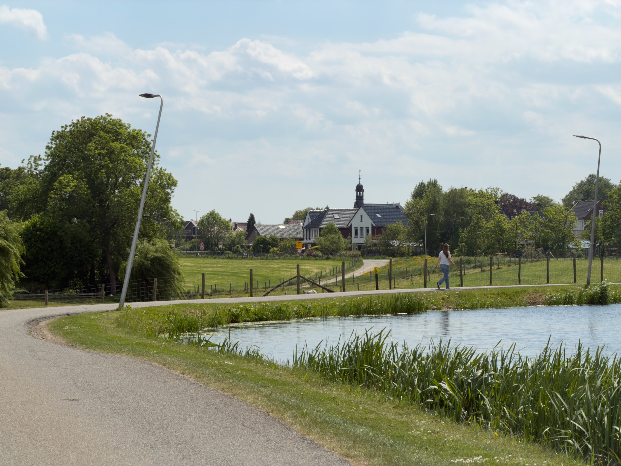 Approach to Aarlanderveen with the village church visible across a green field and a hiker on the path