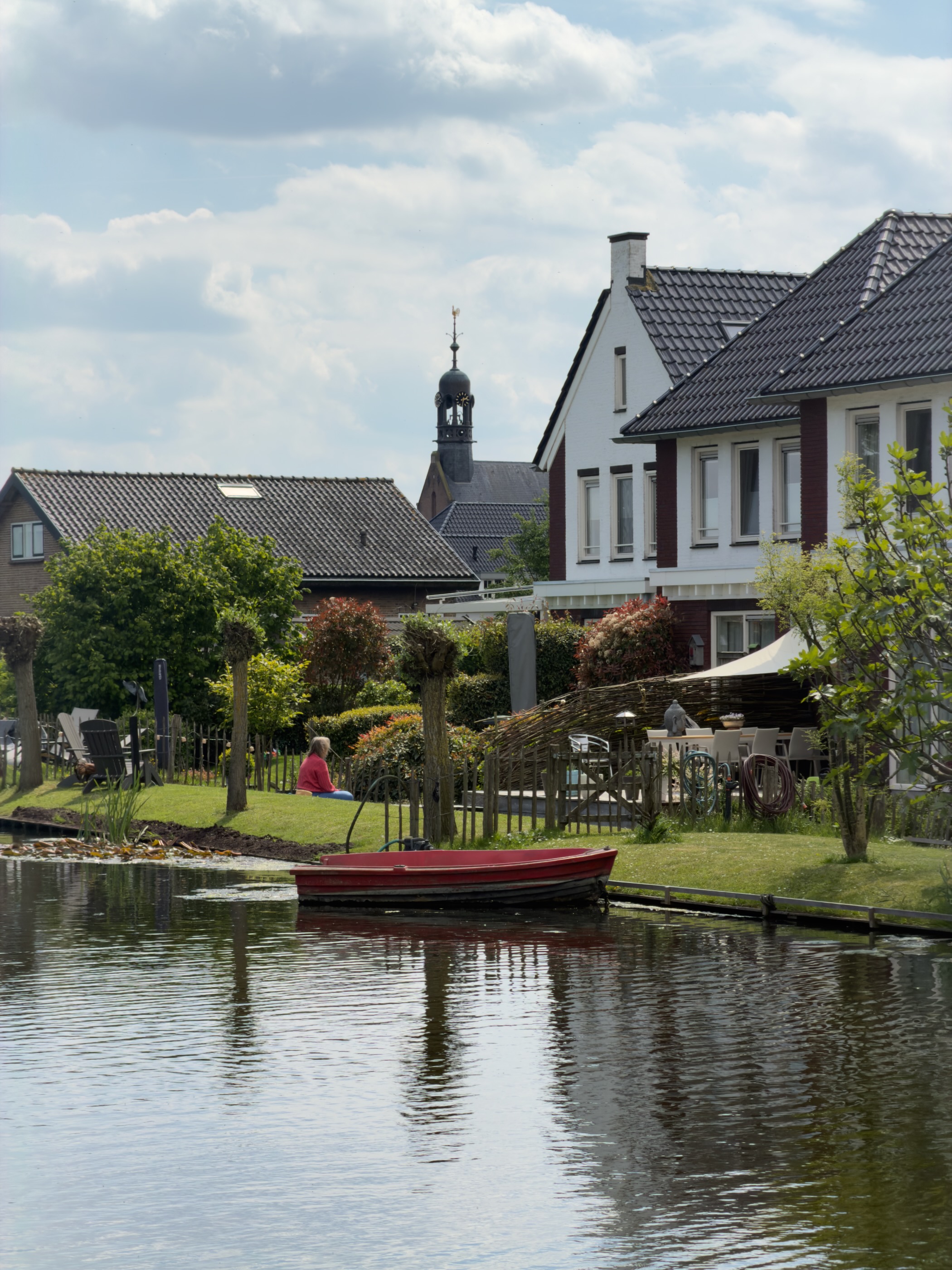 Red rowing boat moored beside a brick house in Aarlanderveen, with the church spire rising behind