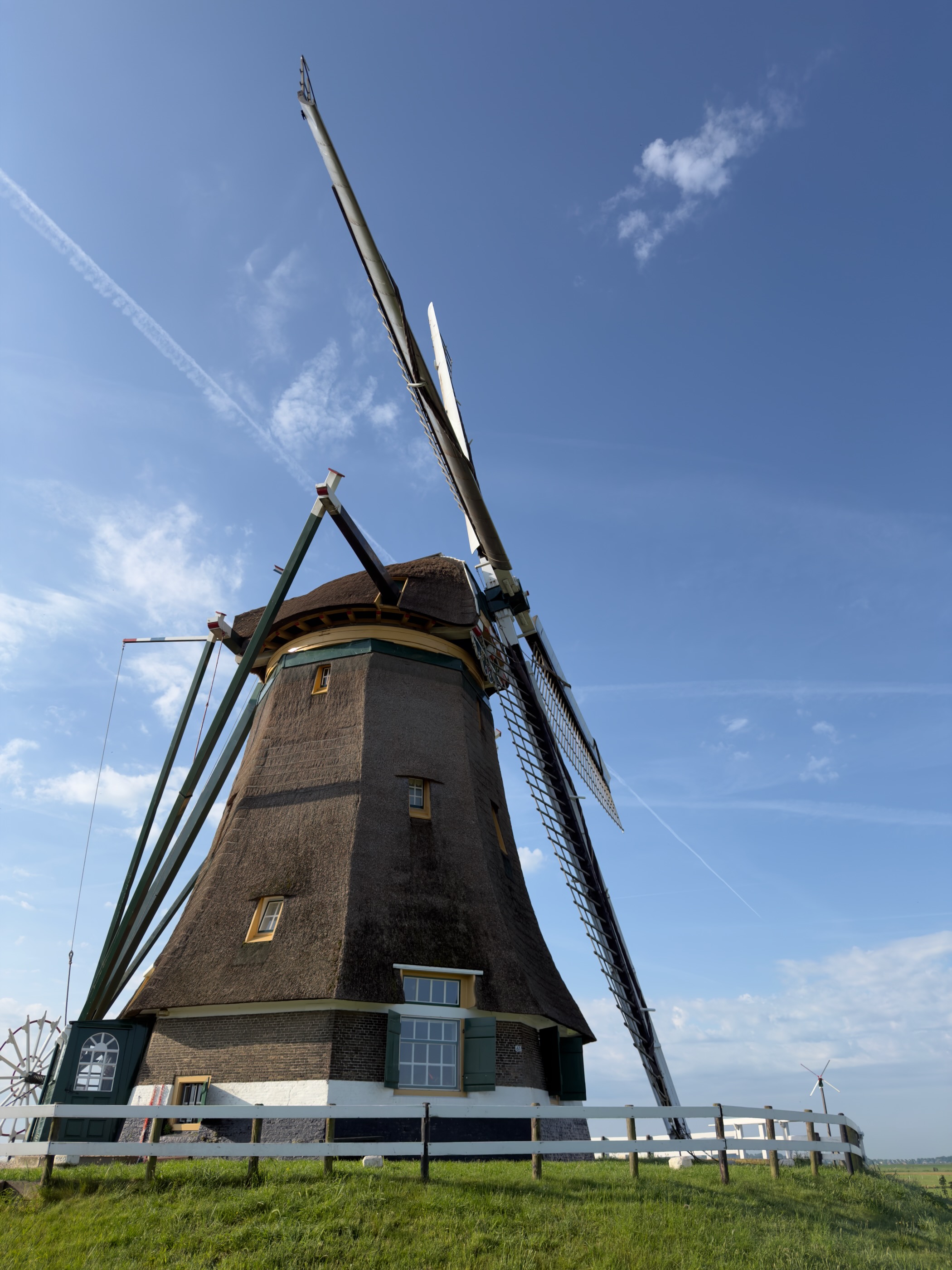 Tall thatched windmill of the Aarlanderveen complex seen from below against a deep blue sky, a white fence at its base