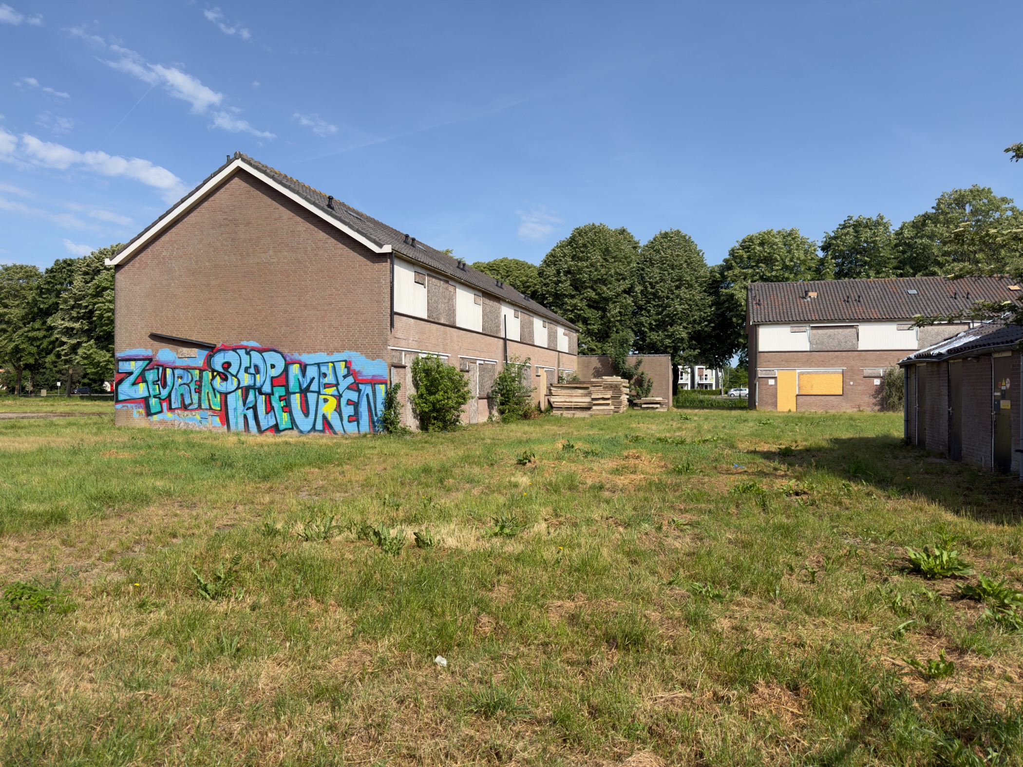 Row of brick houses with a colourful graffiti mural on a low wall in a rough grassy clearing