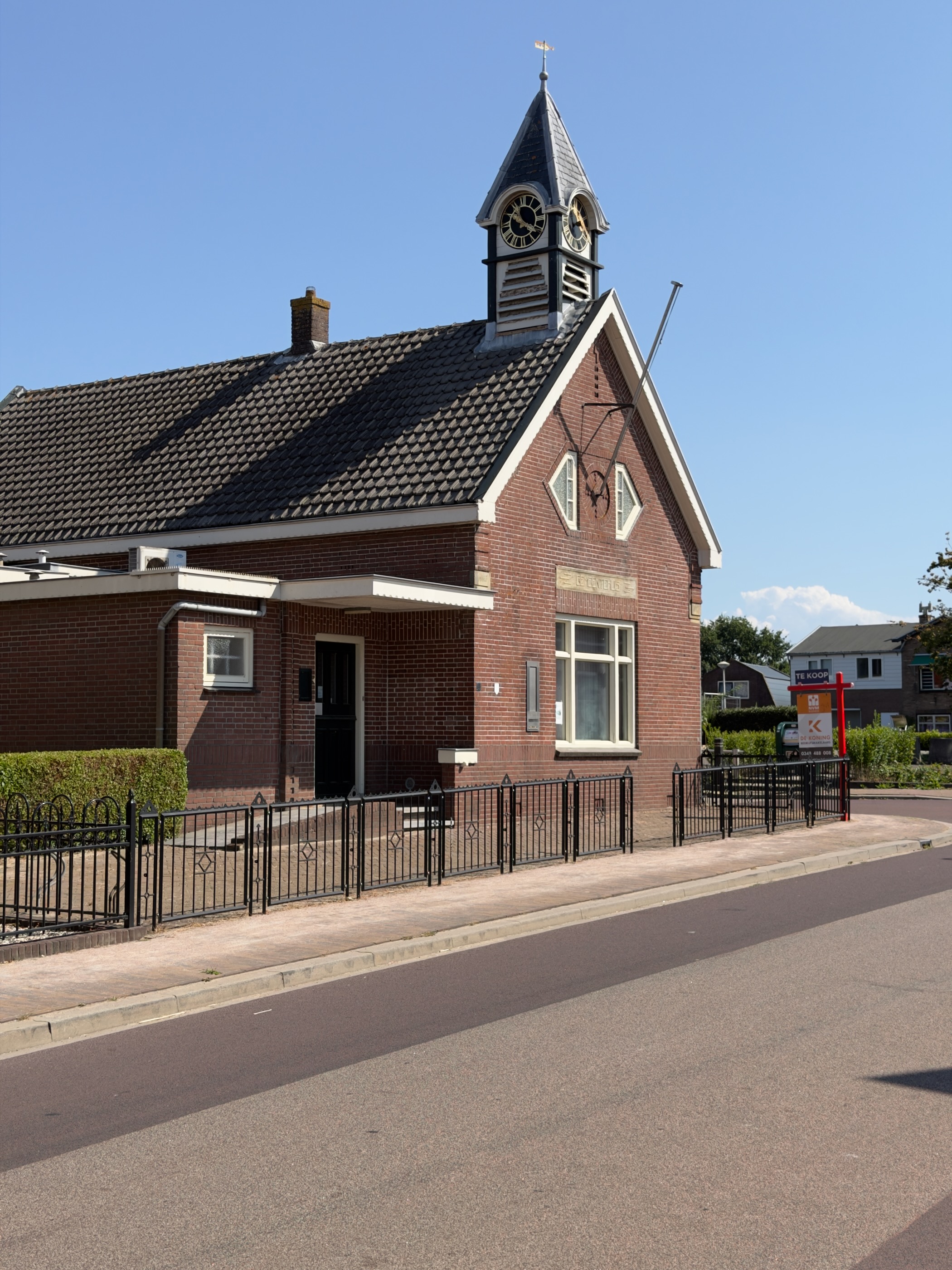Brick building with a small clock tower and the name Lekdijk above the window, behind a black iron fence